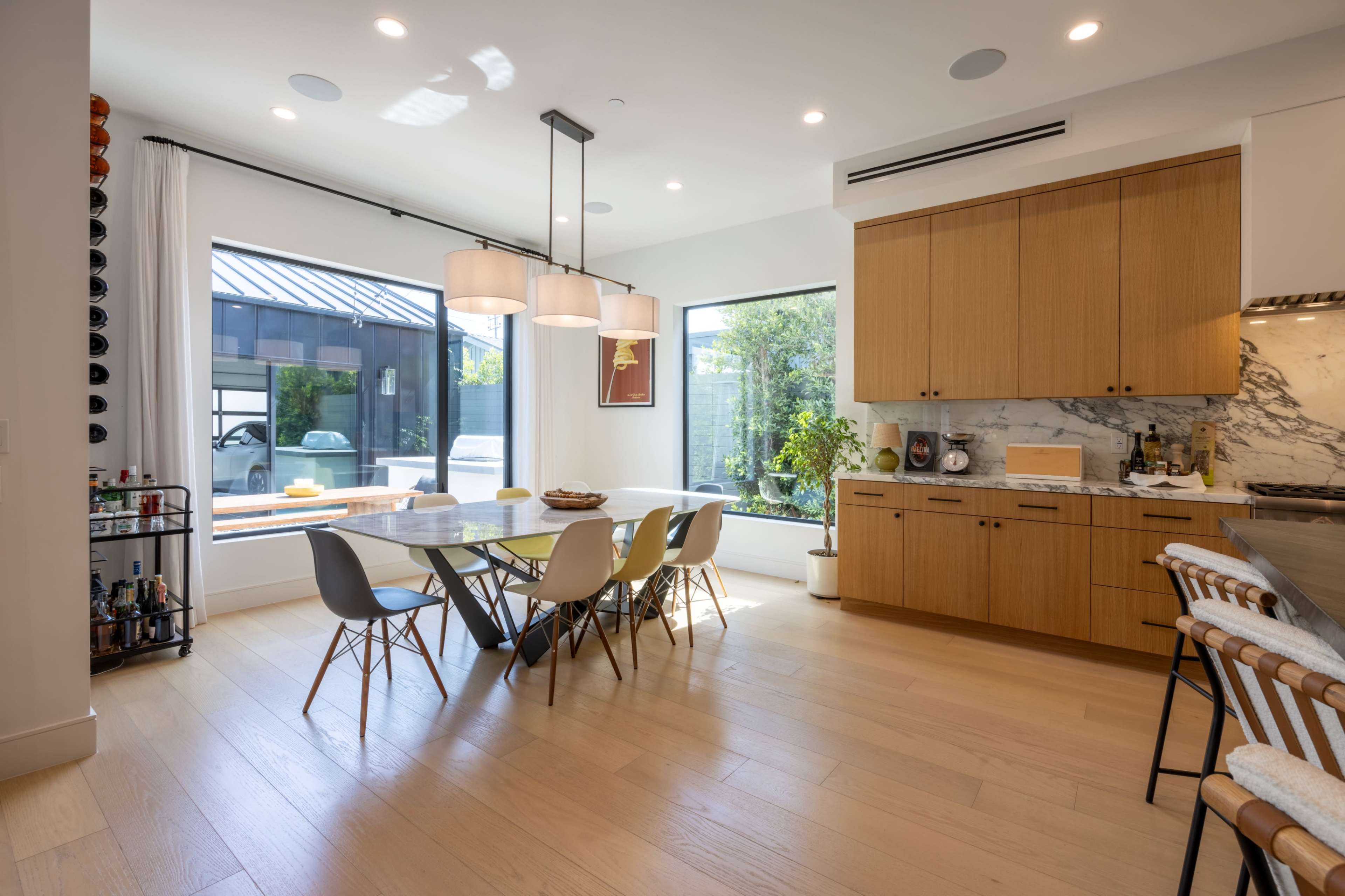 A modern kitchen and dining area with a large table, chairs, and windows overlooking a garden.