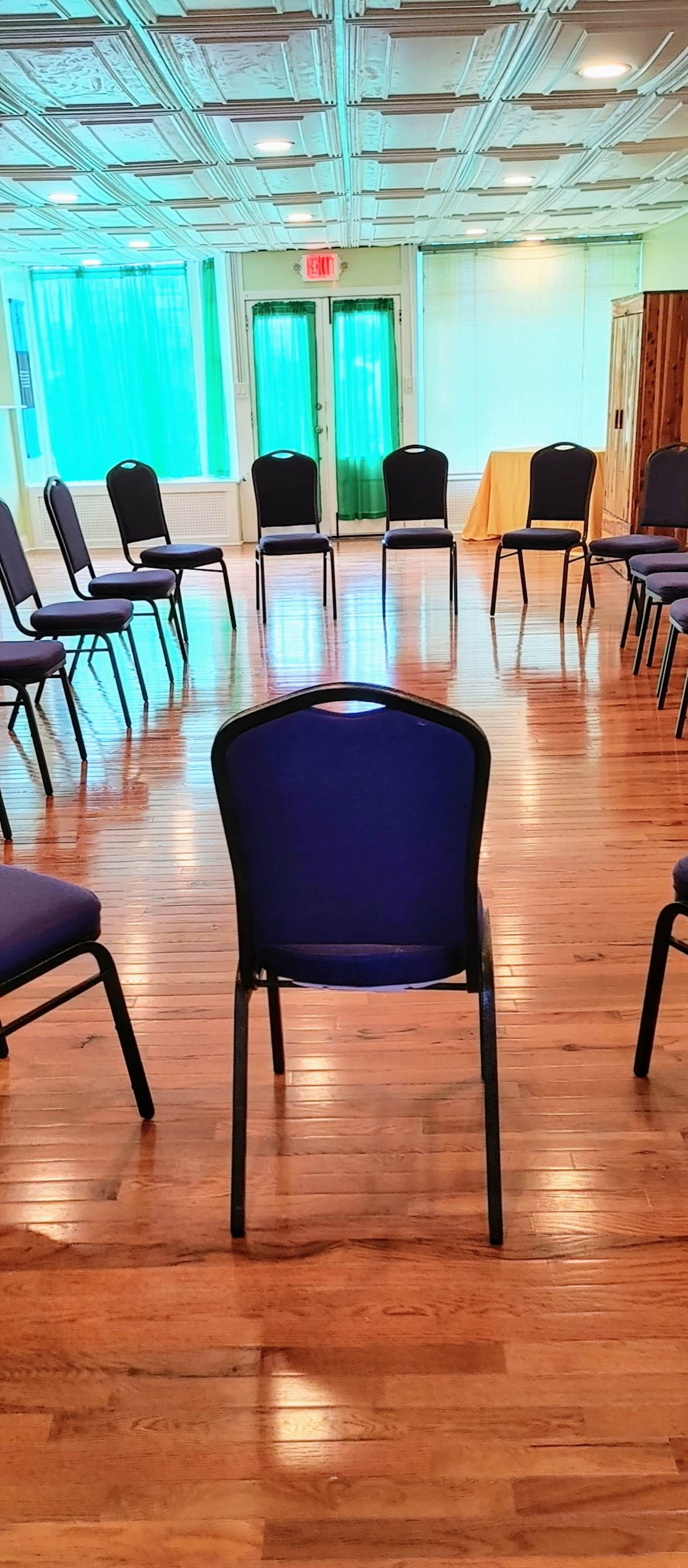 A circle of empty chairs is arranged on a wooden floor in a well-lit room.