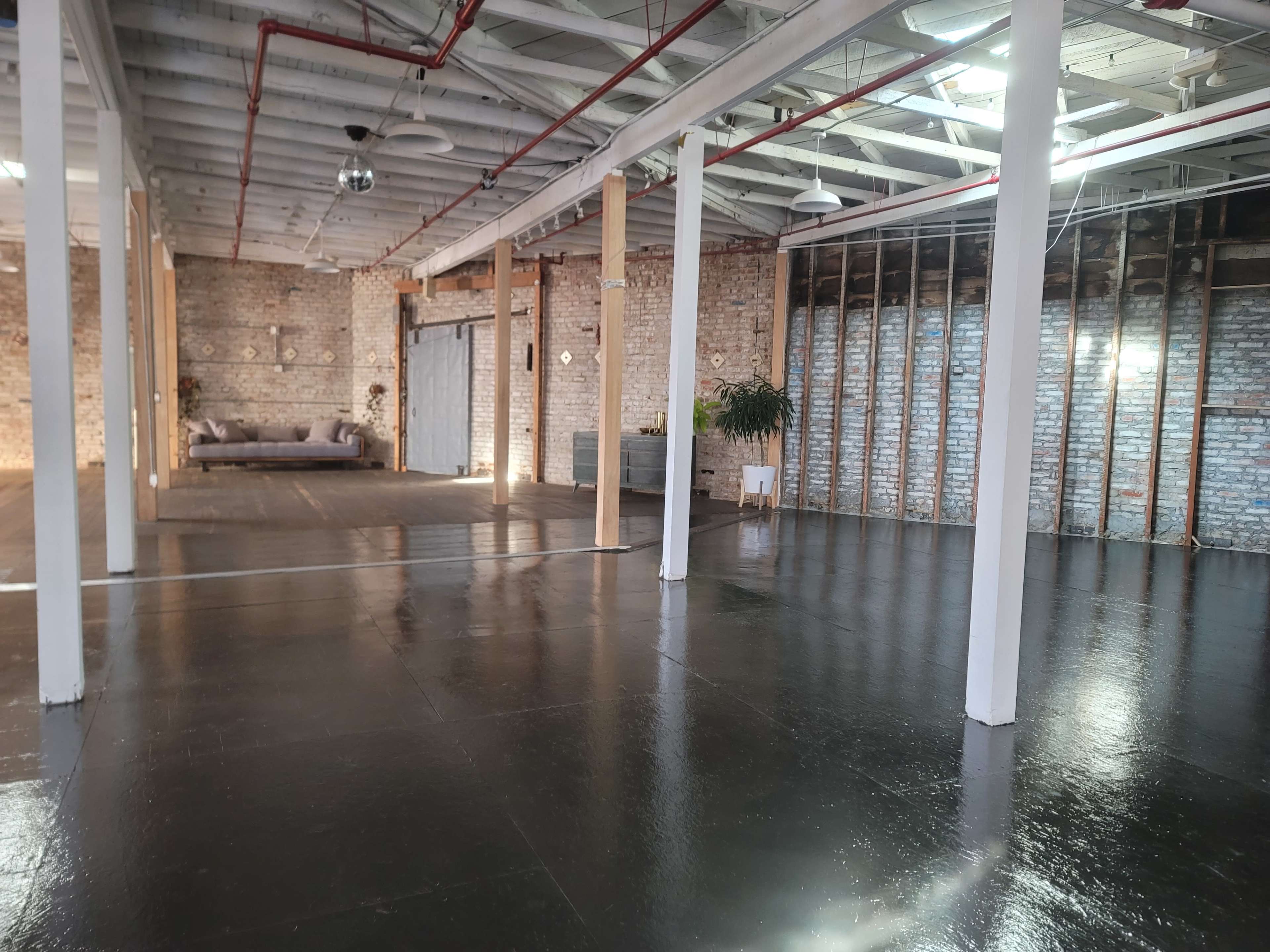 A spacious, industrial-style interior with a polished floor, exposed brick walls, and columns supporting the ceiling.
