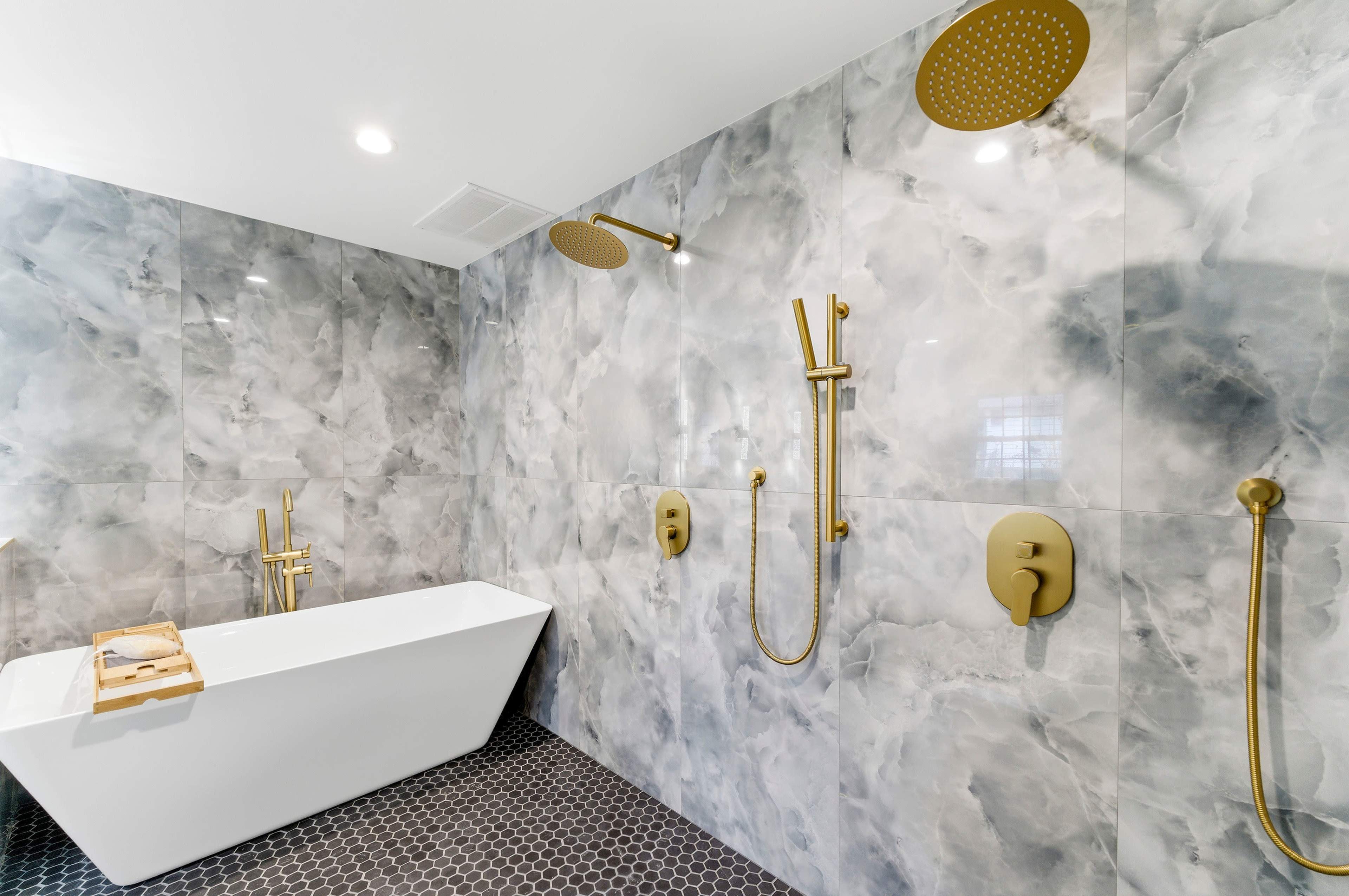 The image shows a modern bathroom featuring a freestanding white bathtub, gray marble walls, and gold fixtures.