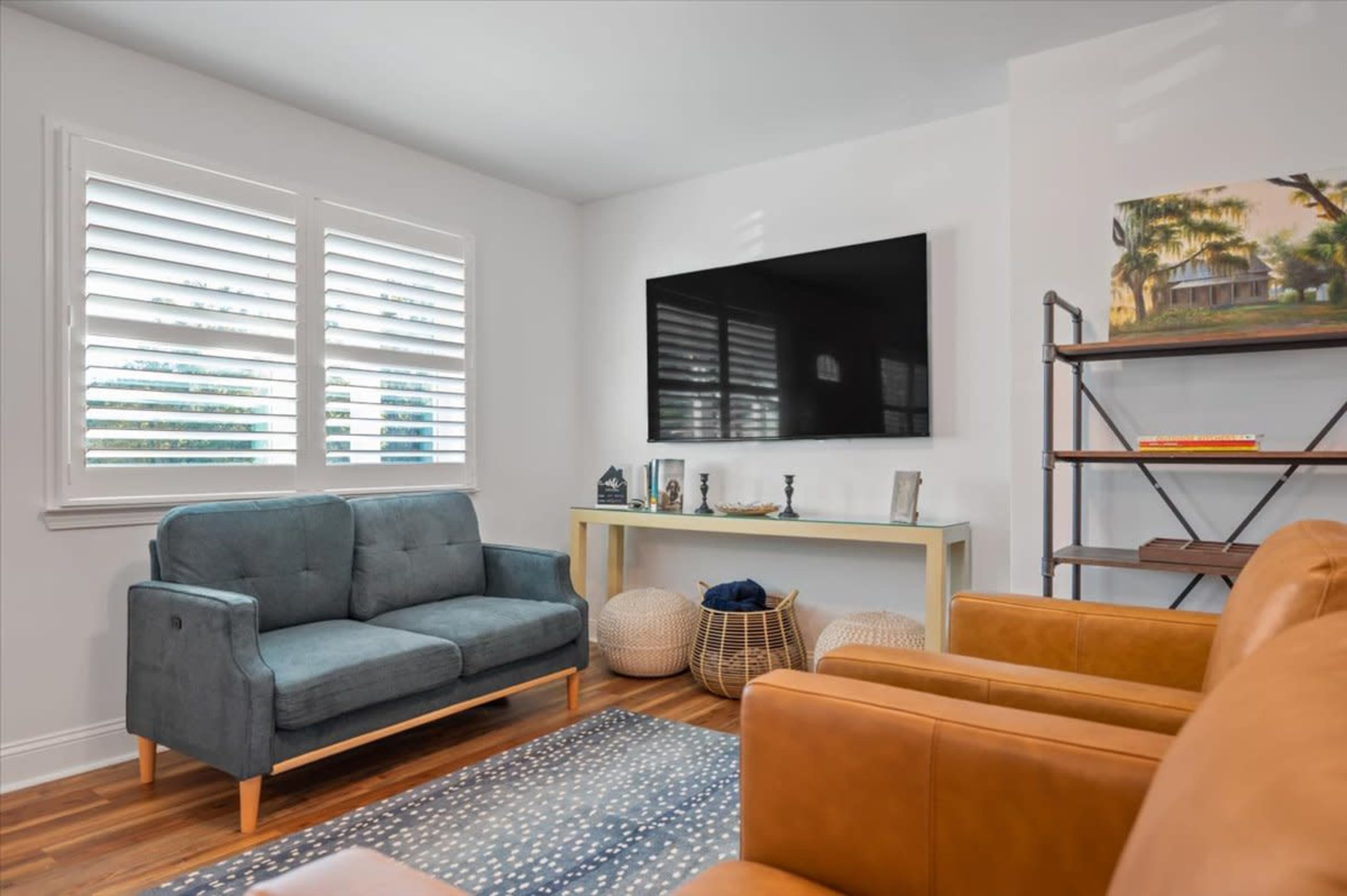 The living room features a gray sofa, two brown armchairs, a large television mounted on the wall, and a shelf with decorative items.