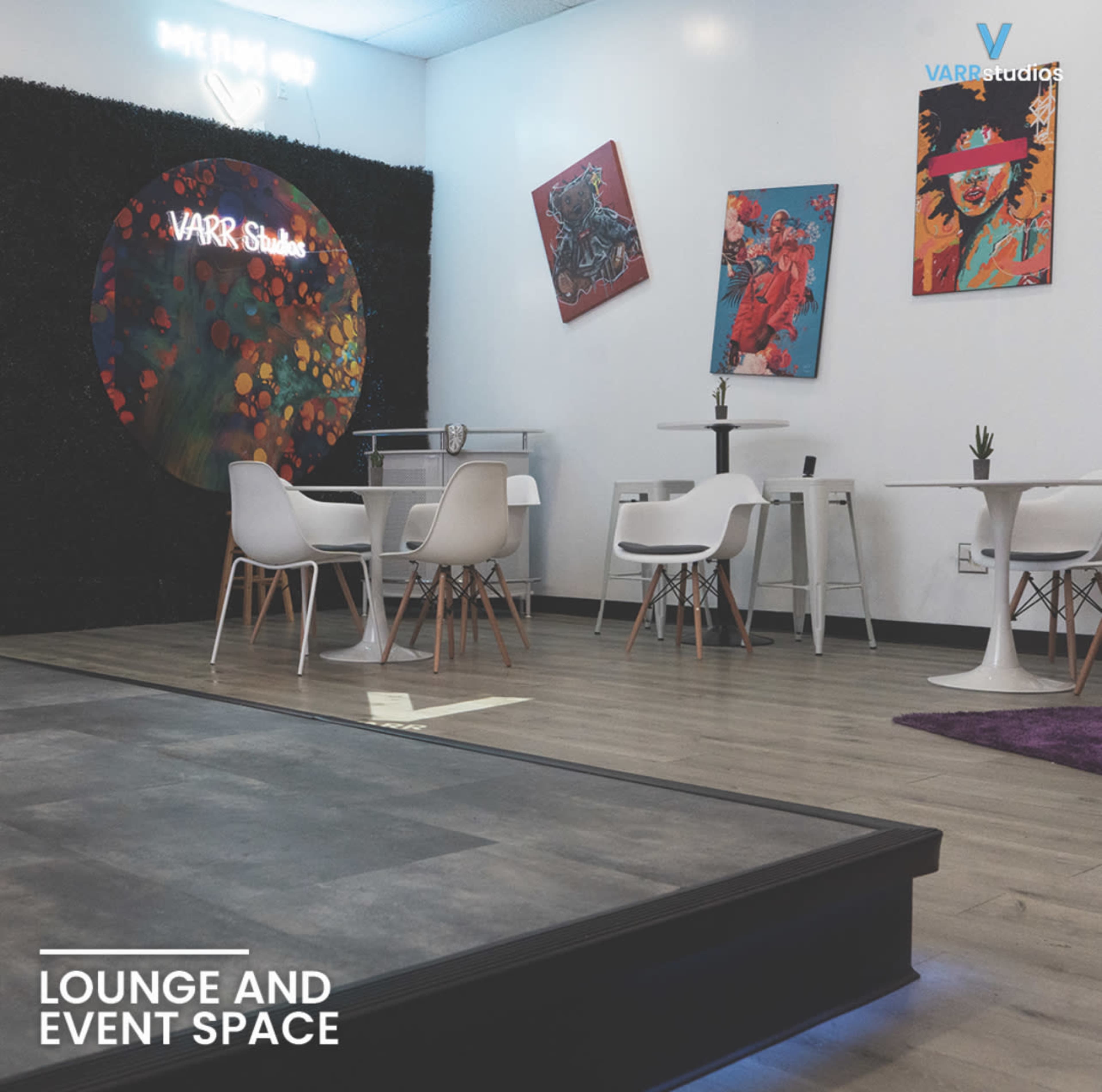 A modern lounge and event space with white chairs, small tables, and colorful artwork on the walls.