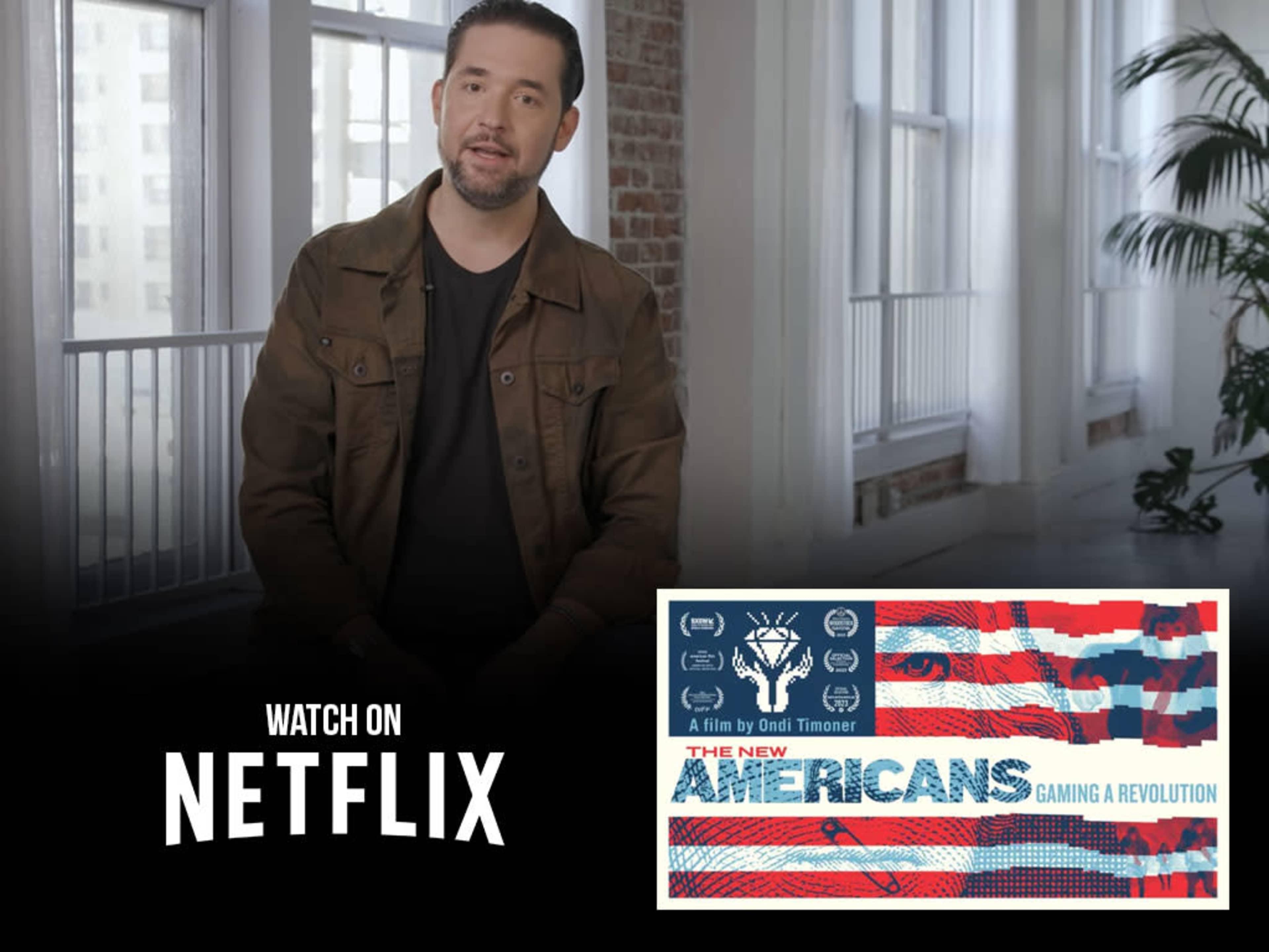 A man is speaking in an indoor setting with large windows, next to a promotional graphic for the film "The New Americans: Gaming a Revolution" available on Netflix.