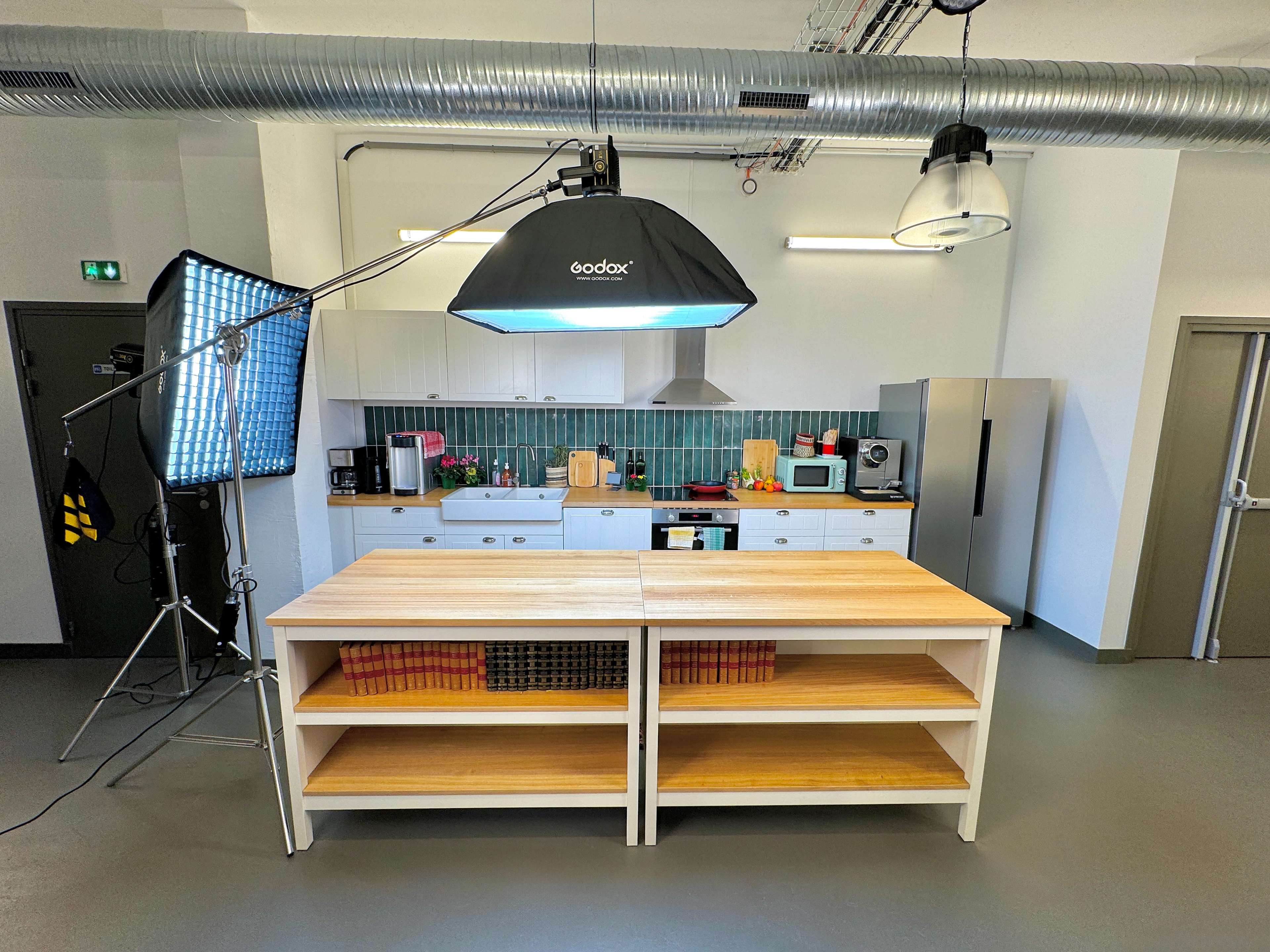 A spacious kitchen with modern appliances, featuring a central wooden preparation table and ample lighting set up for photography.