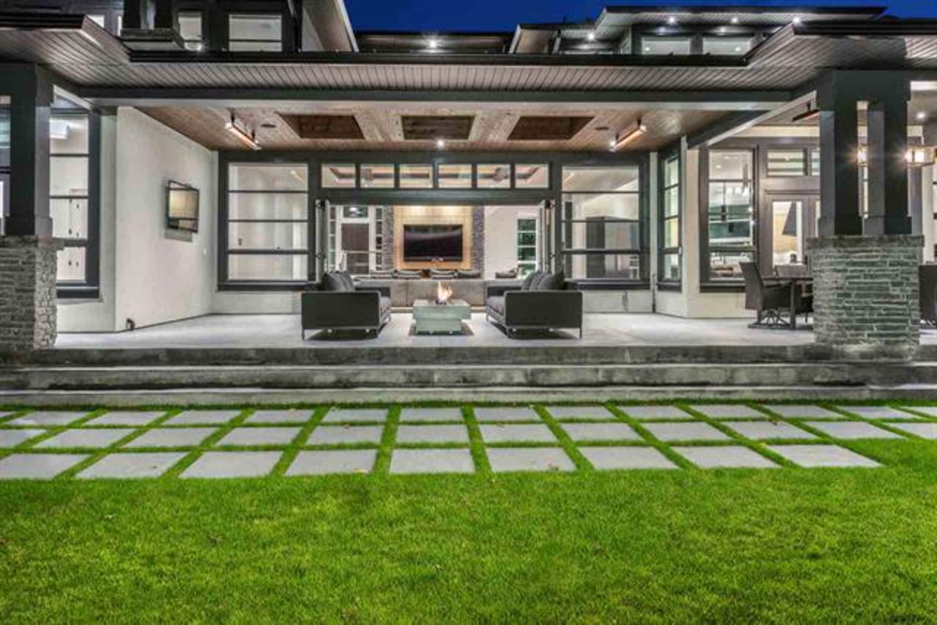 A modern home with a spacious outdoor patio, featuring seating areas and a neatly manicured lawn with stone pathways.