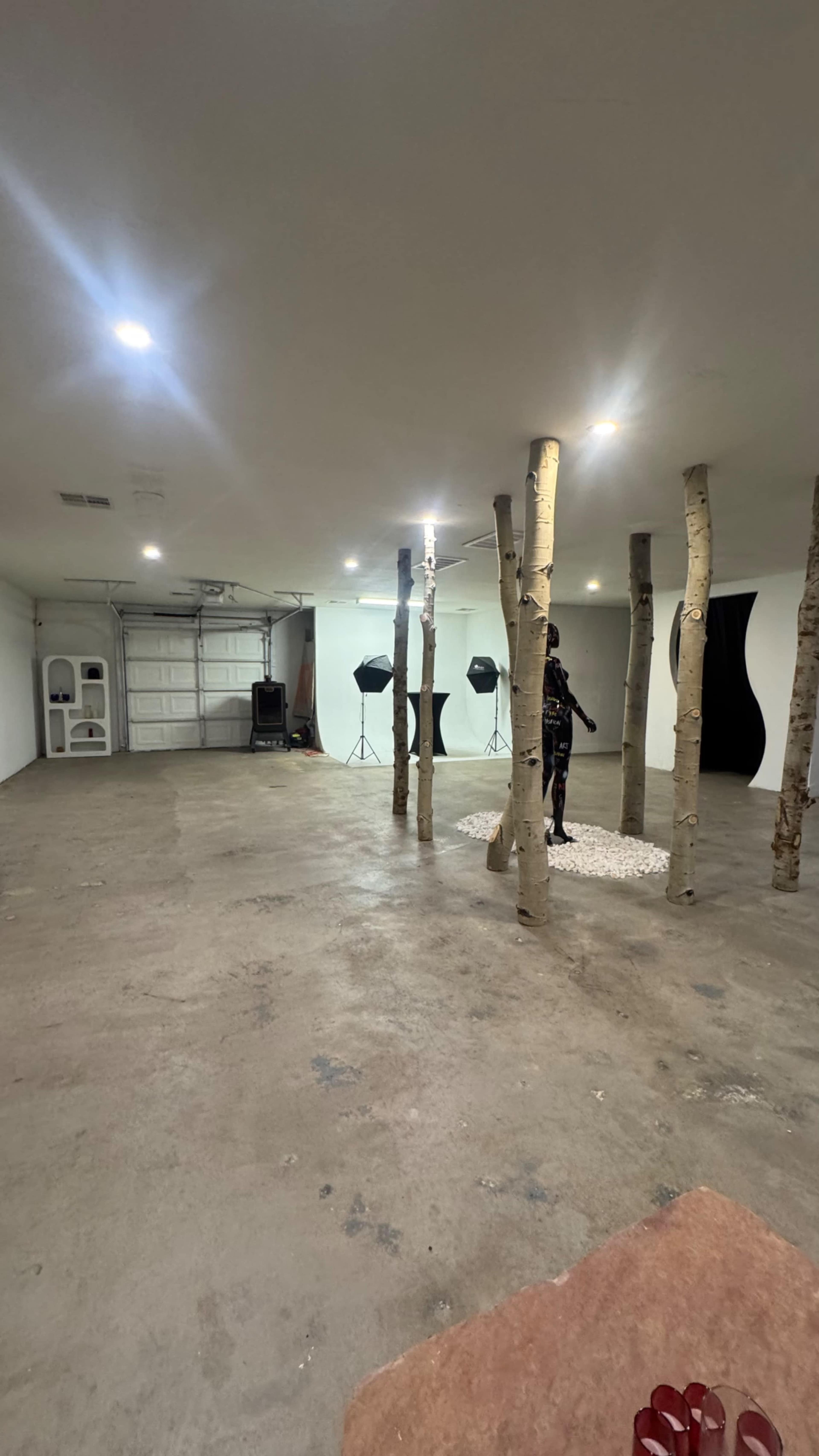The image shows a spacious indoor area with several tree-like poles, a rocky base, and various lighting equipment in the background.