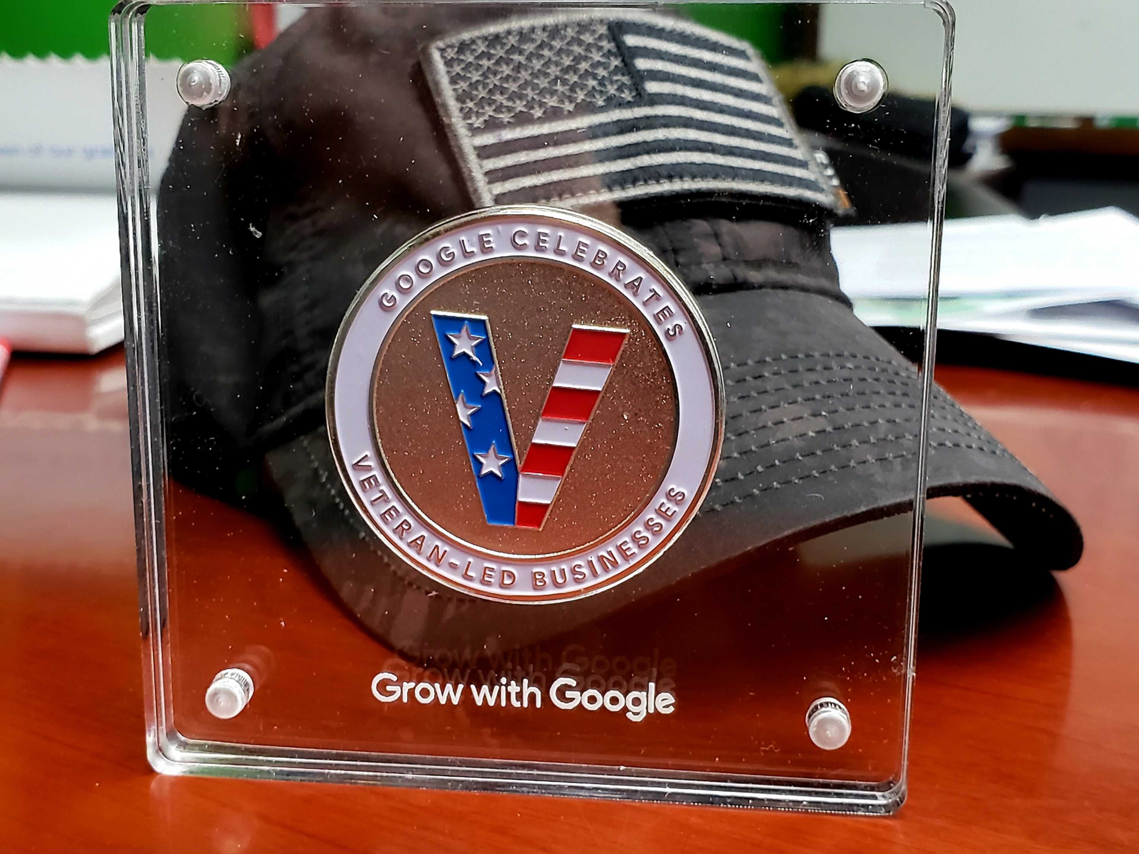 The image features a clear plaque celebrating veteran-led businesses alongside a black cap adorned with an American flag.