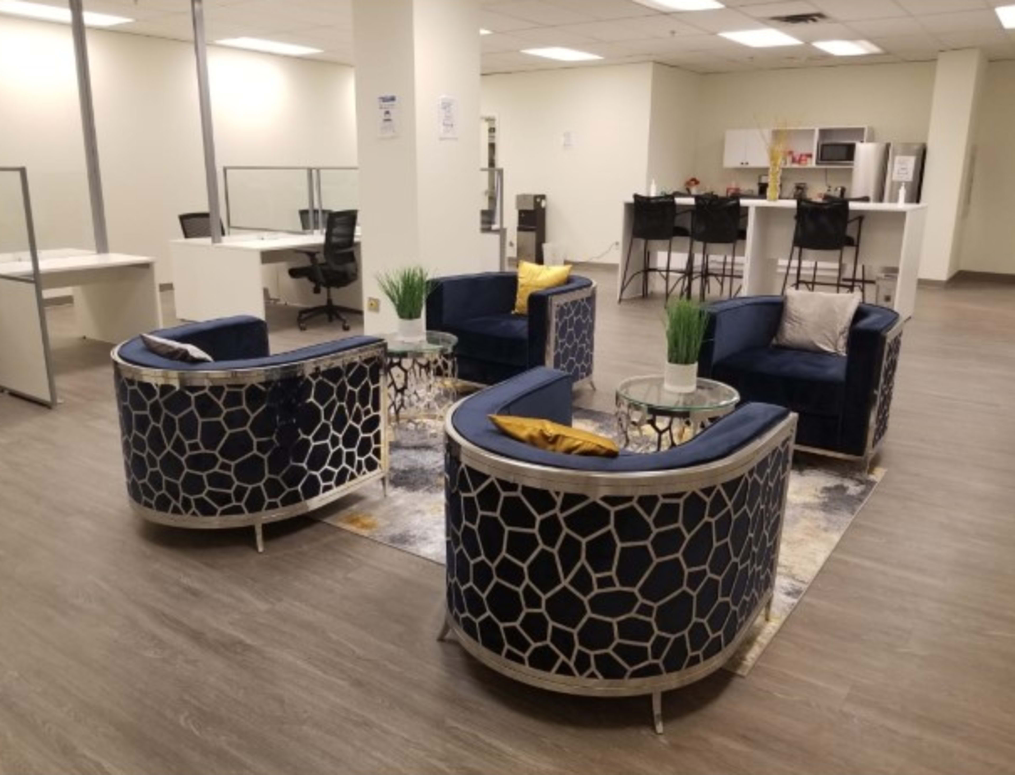 A modern office space features four circular chairs arranged around a small table, with a kitchenette visible in the background.