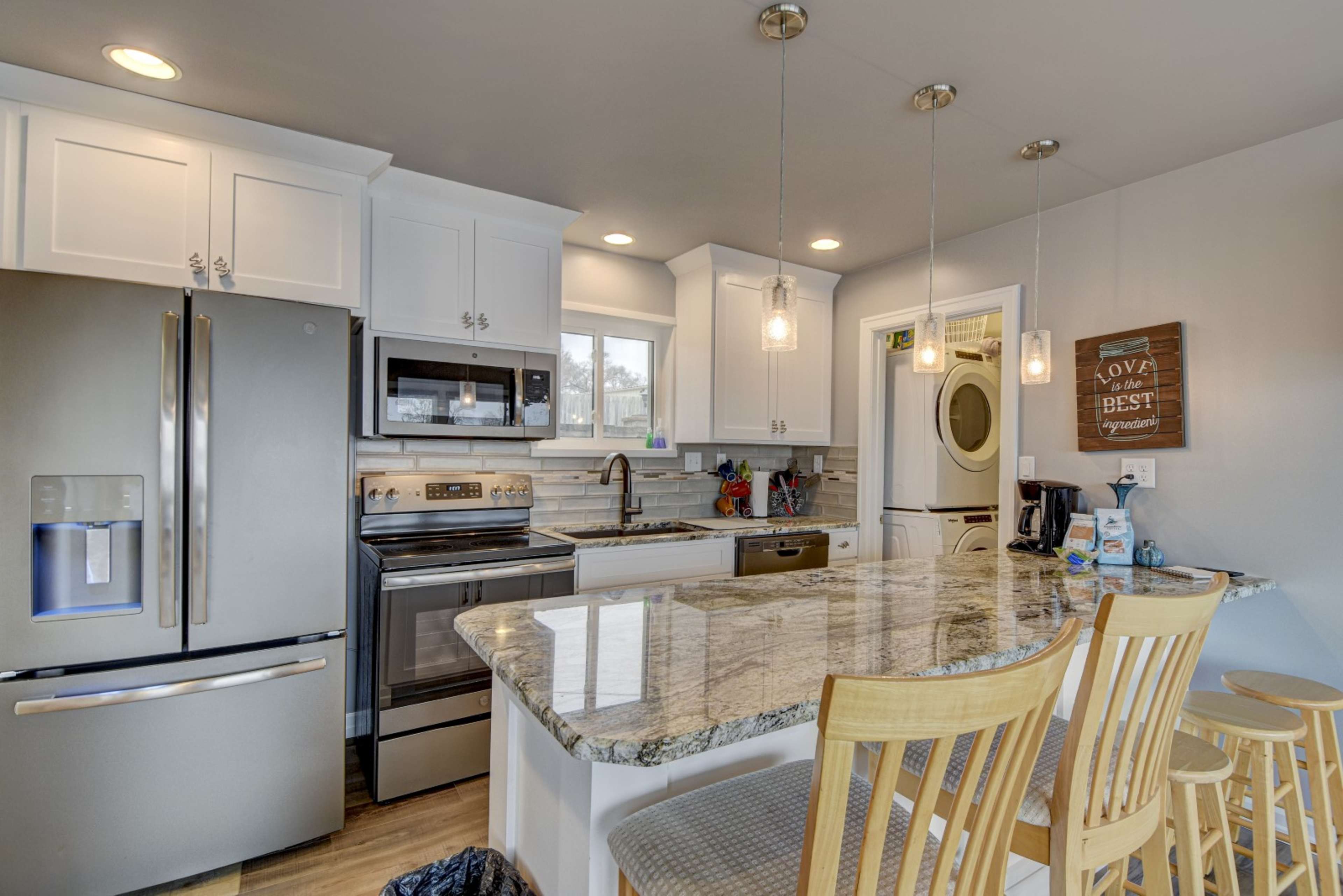 A modern kitchen with white cabinetry, stainless steel appliances, a granite countertop, and bar seating.