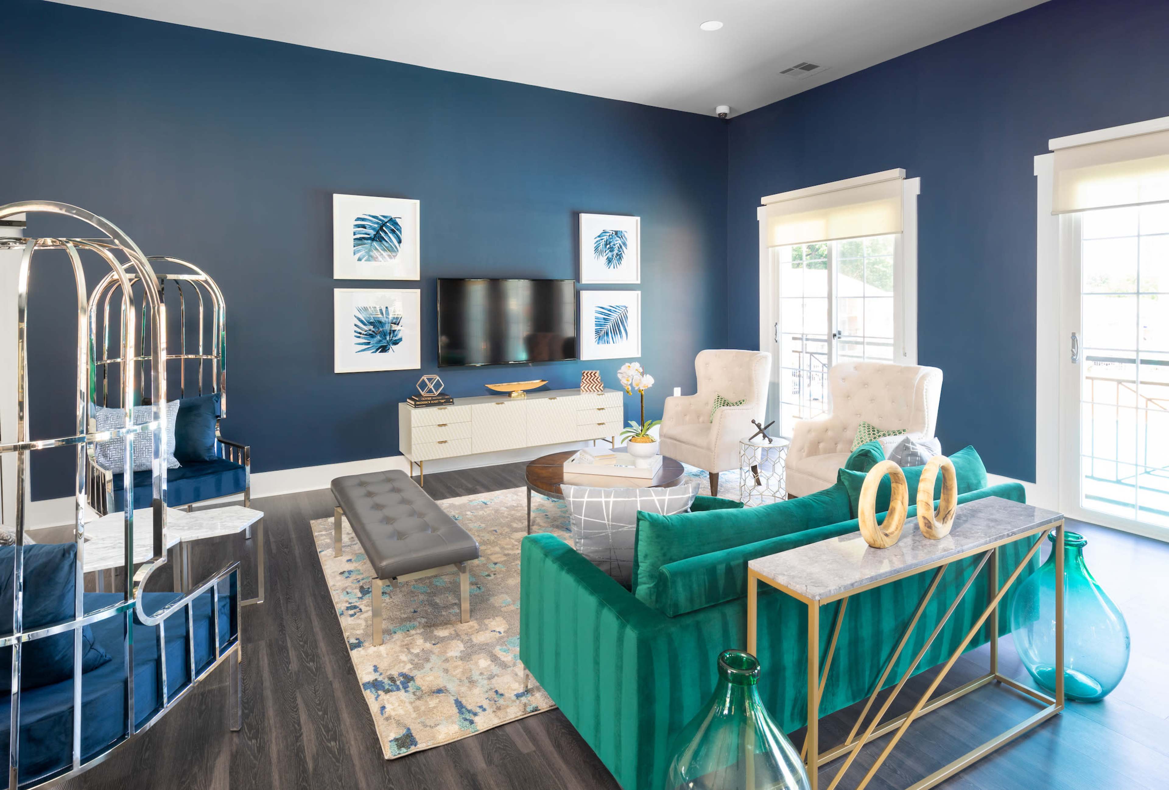 A modern living room features blue walls, a large television mounted on the wall, plush seating, and decorative accessories on a coffee table.