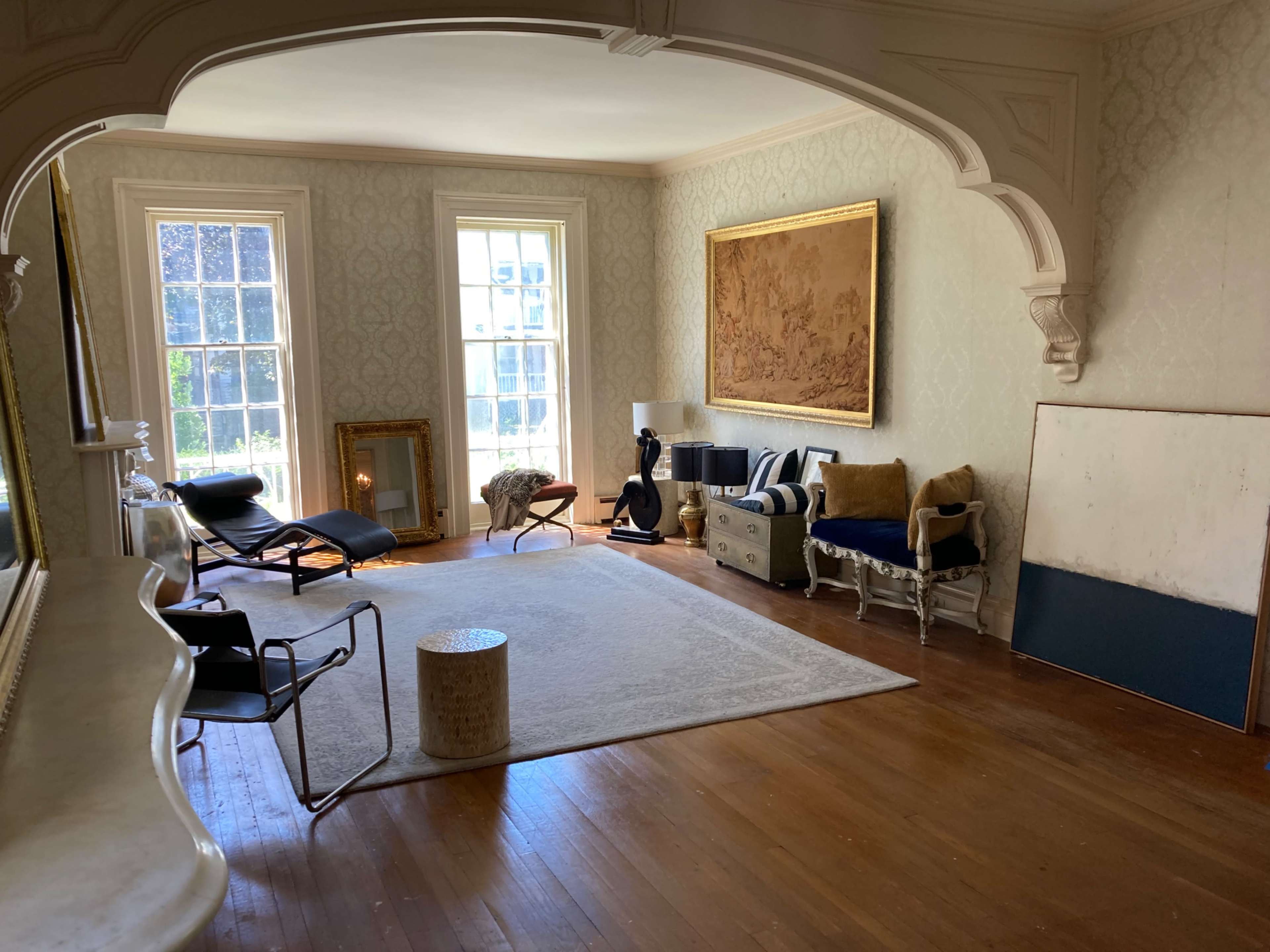 The room features hardwood floors, large windows, a framed wall art piece, and a mix of modern and classic furniture.