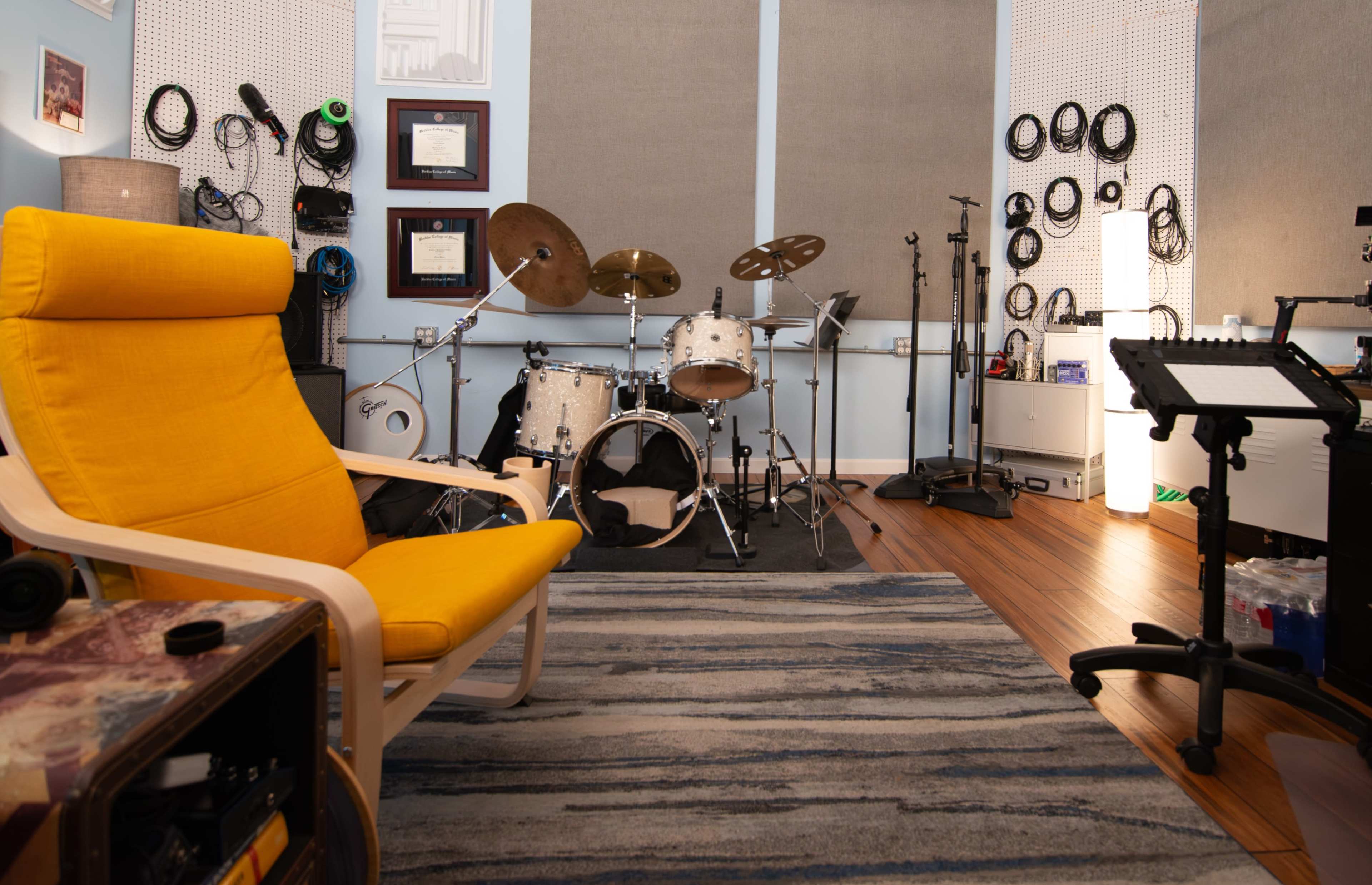 A cozy music studio features a yellow chair, a drum set, and various music equipment arranged in a well-organized space.