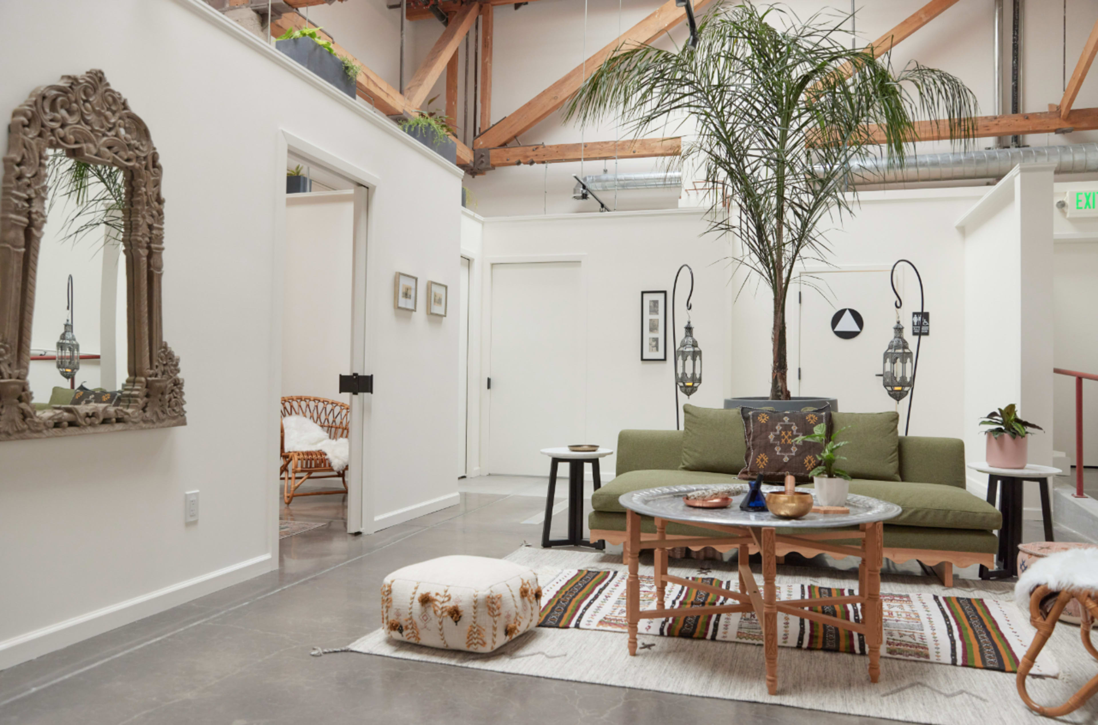 A modern interior space with a green sofa, a round coffee table, decorative plants, and artistic elements on the walls.