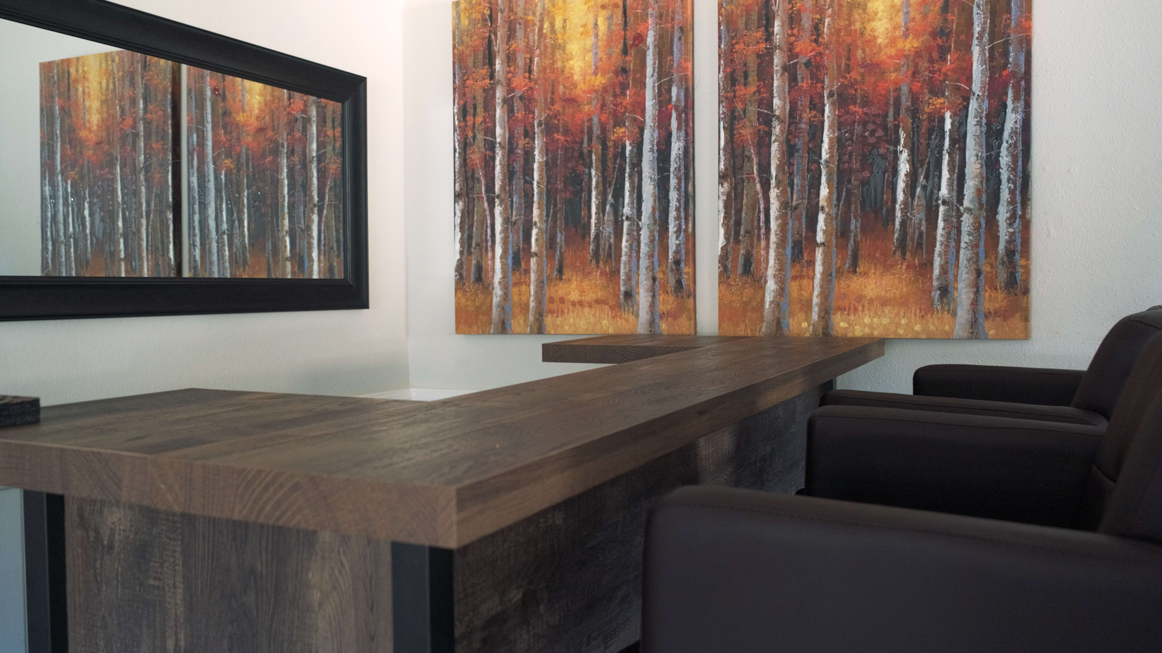 A modern interior with a wooden desk and two brown chairs set against a backdrop of two large paintings of autumn trees.