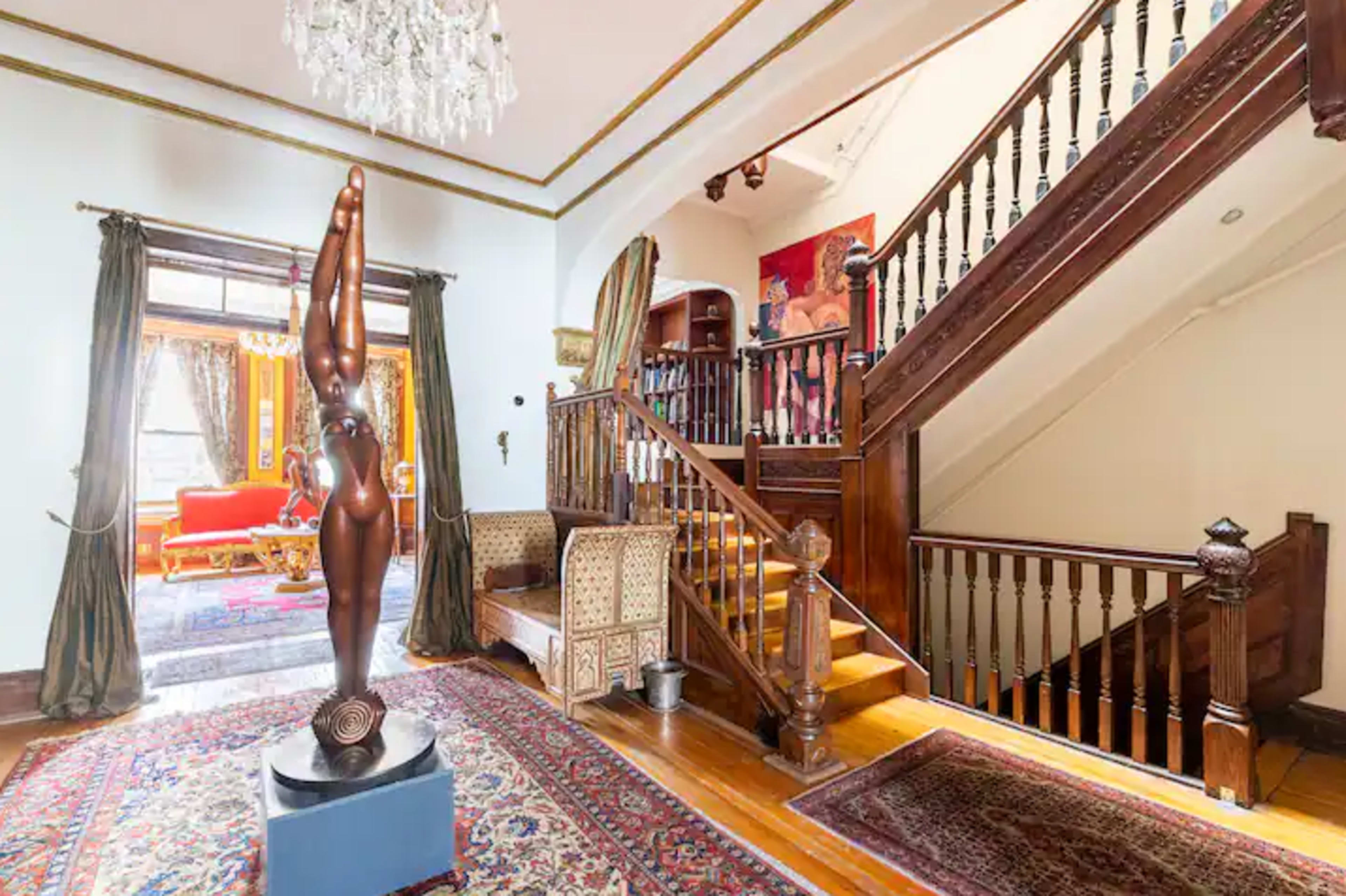 A wooden staircase leads to an upper level, with a decorative sculpture and couch visible in an adjacent room.
