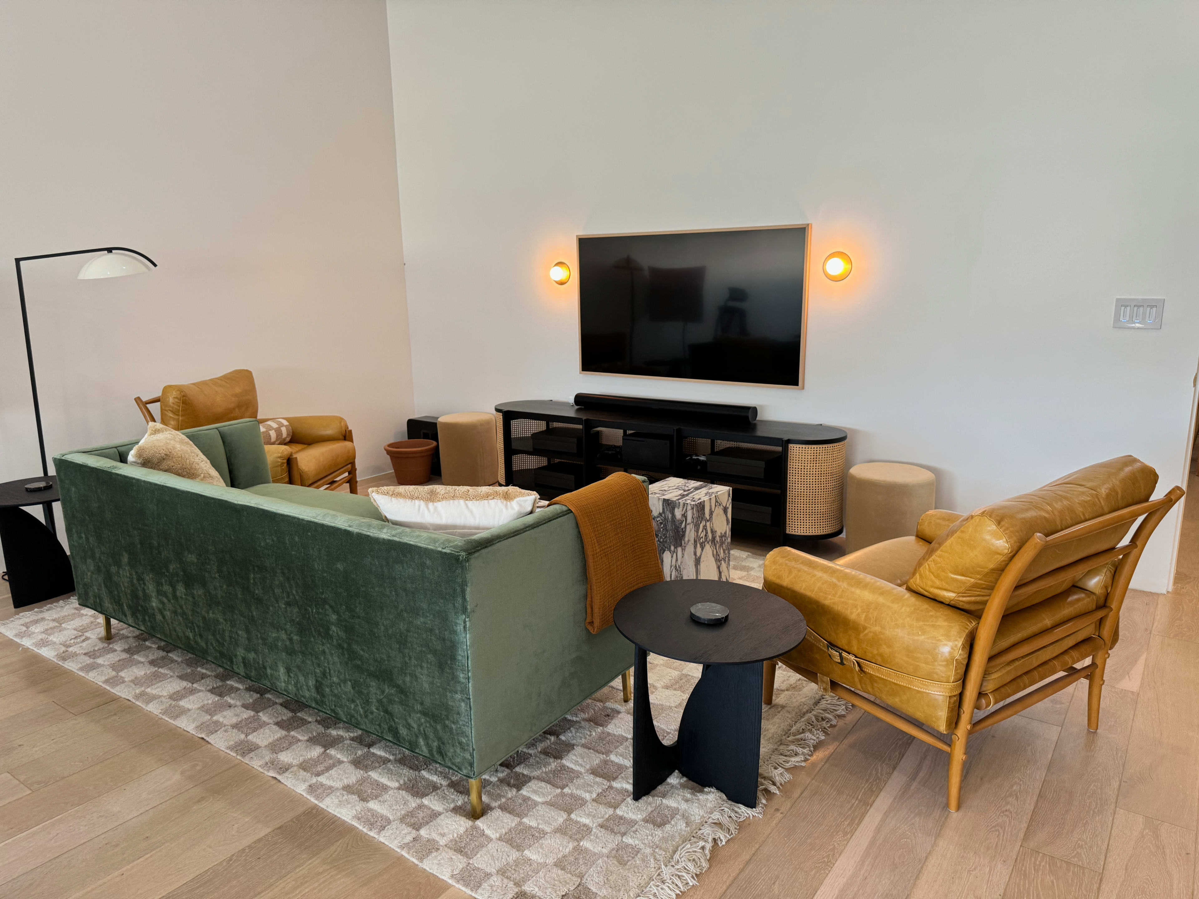 A modern living room featuring a green velvet sofa, a yellow leather chair, a black coffee table, and a mounted television on a white wall.