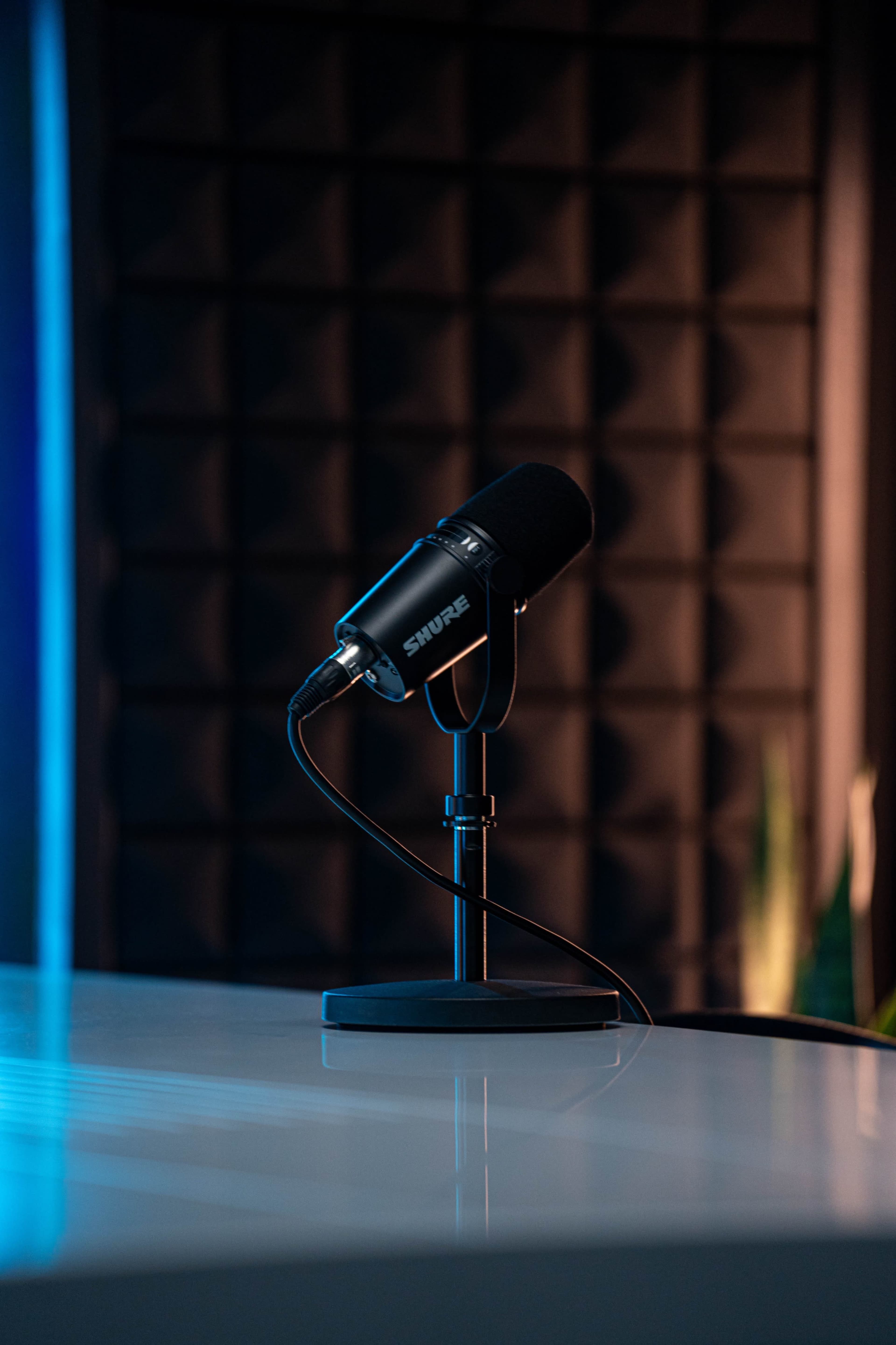A black microphone on a stand is positioned on a table with a textured soundproof wall in the background.