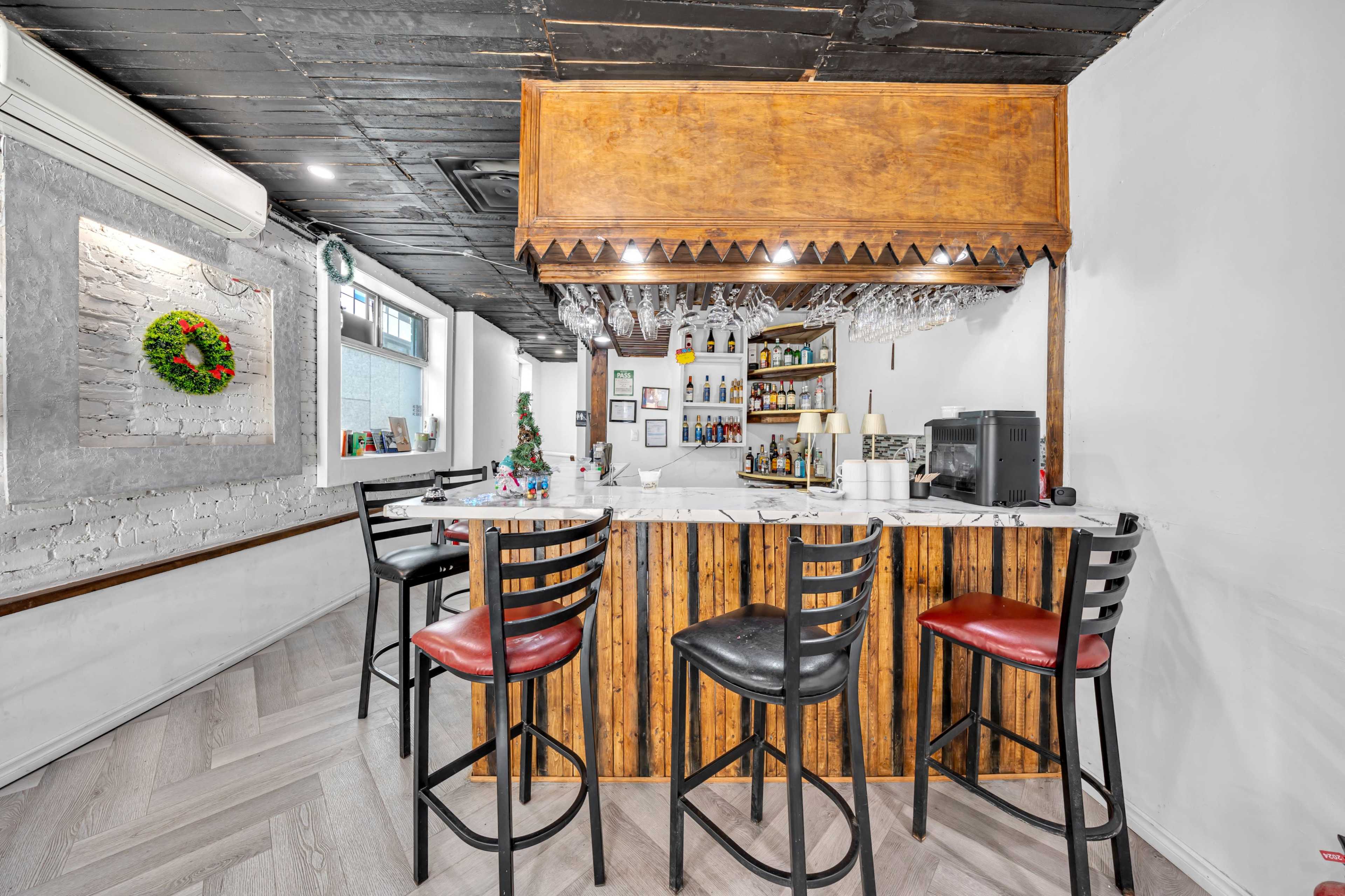 The image shows a bar area with wooden paneling, high stools, and a selection of bottles displayed behind the counter.
