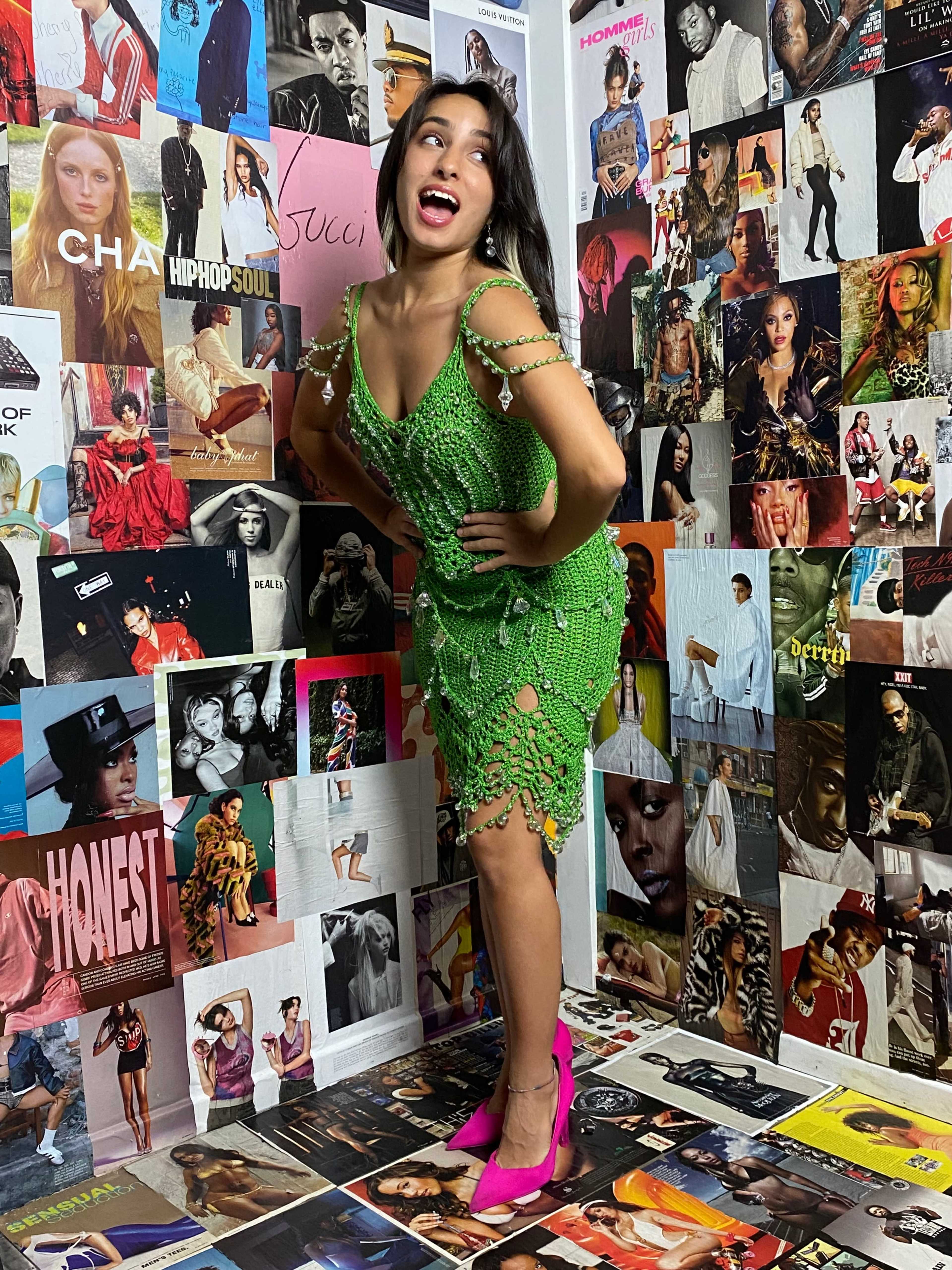 A woman poses playfully in a green crocheted dress against a vibrant collage of magazine covers and fashion posters.