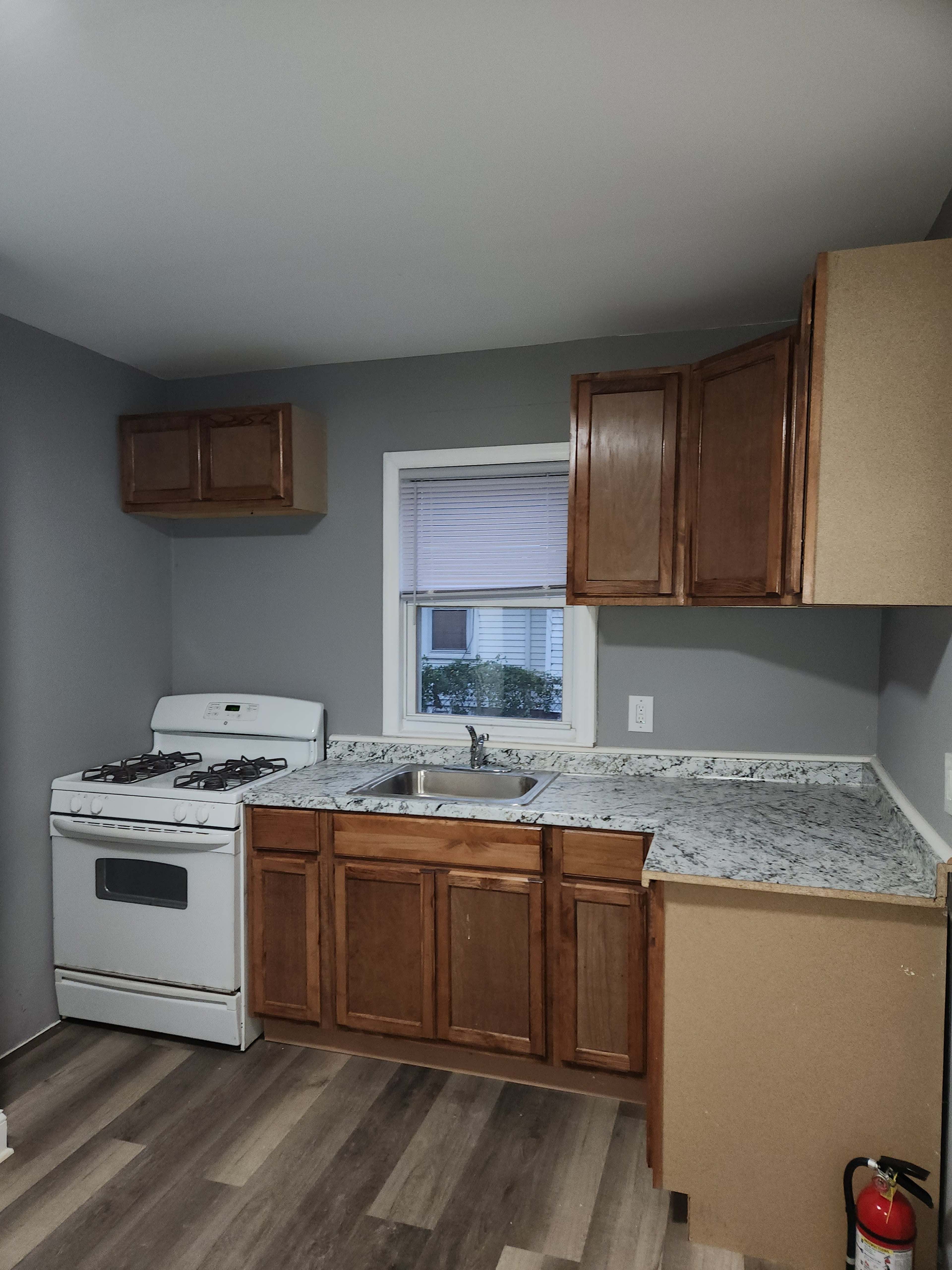 A kitchen featuring wooden cabinets, a countertop with a speckled finish, a white gas stove, and a window above the sink.