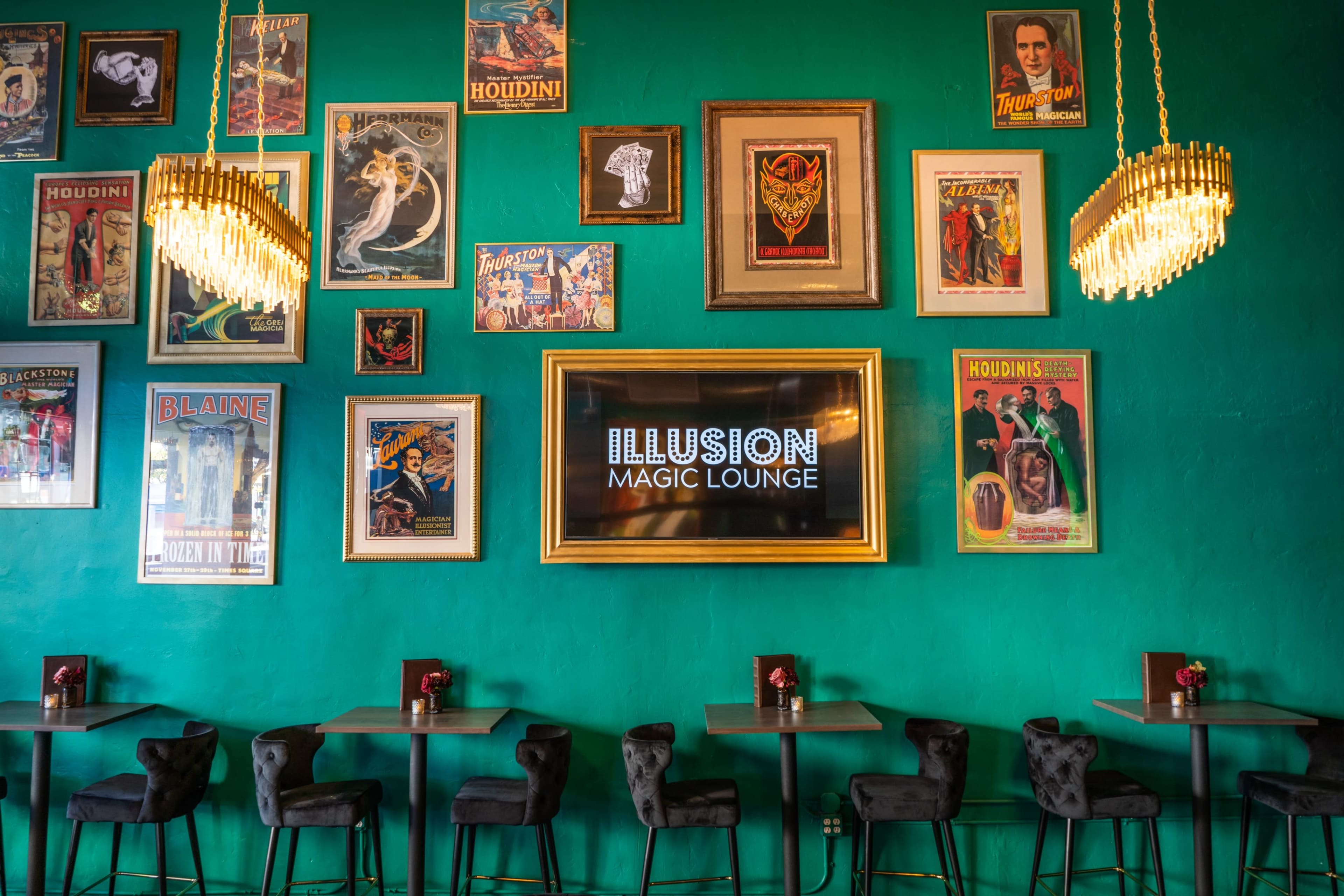 A vibrant green wall adorned with various vintage magic posters, a large illuminated sign reading "ILLUSION MAGIC LOUNGE," and stylish black bar stools at small tables.