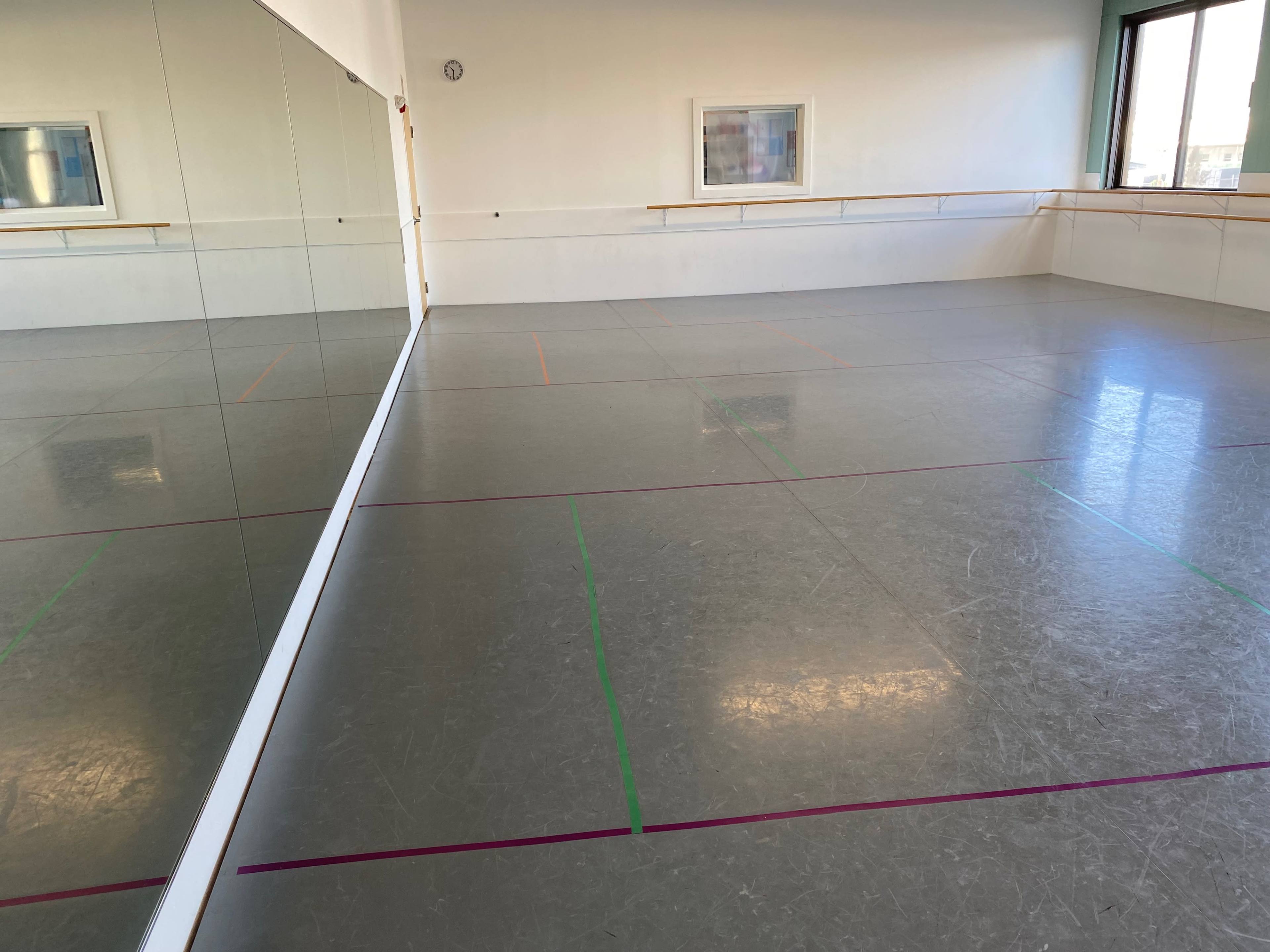 A spacious dance studio with a mirrored wall and colored lines on the floor.