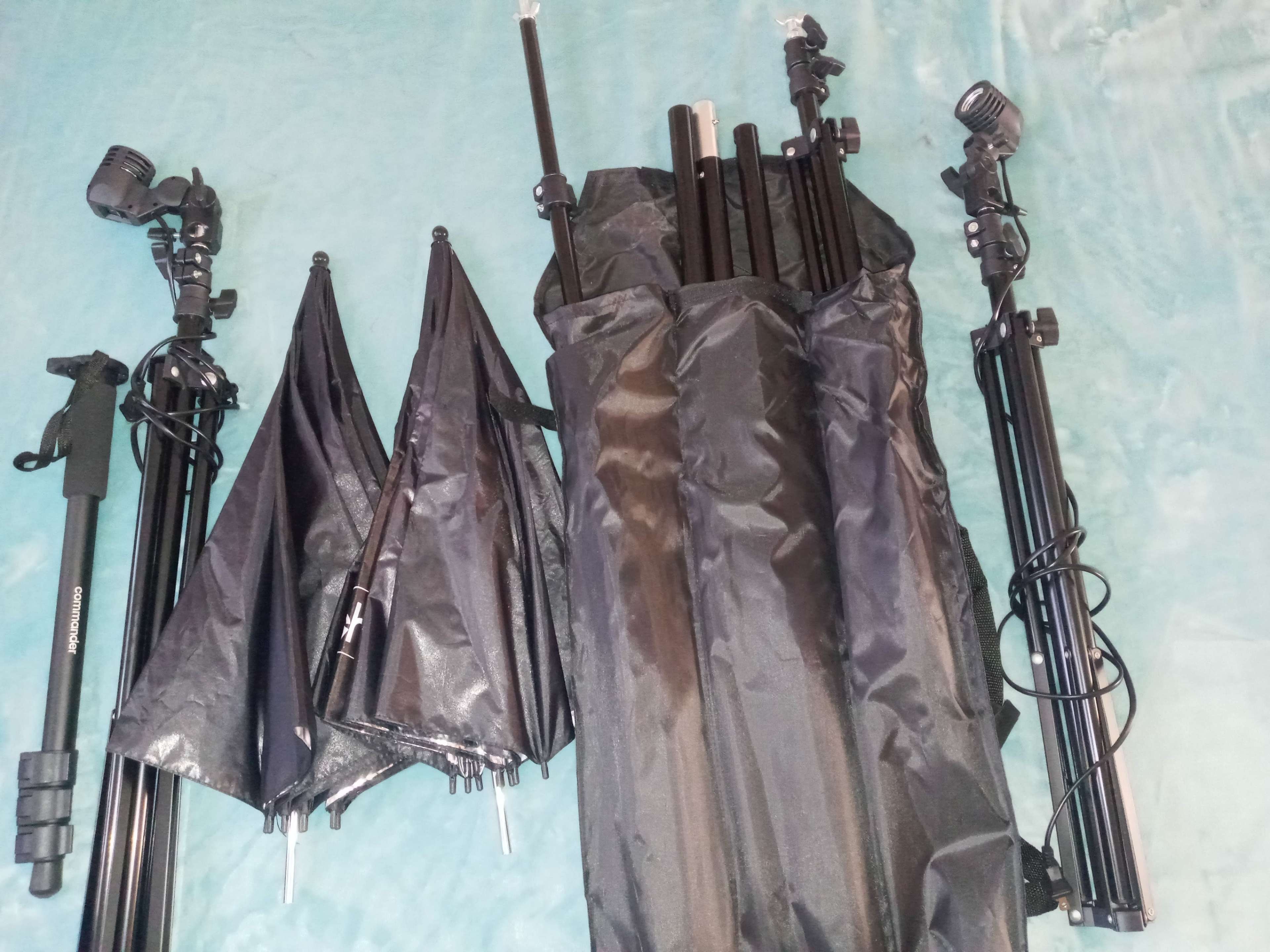 A collection of photography equipment, including black tripods and light stands, arranged next to a storage bag.
