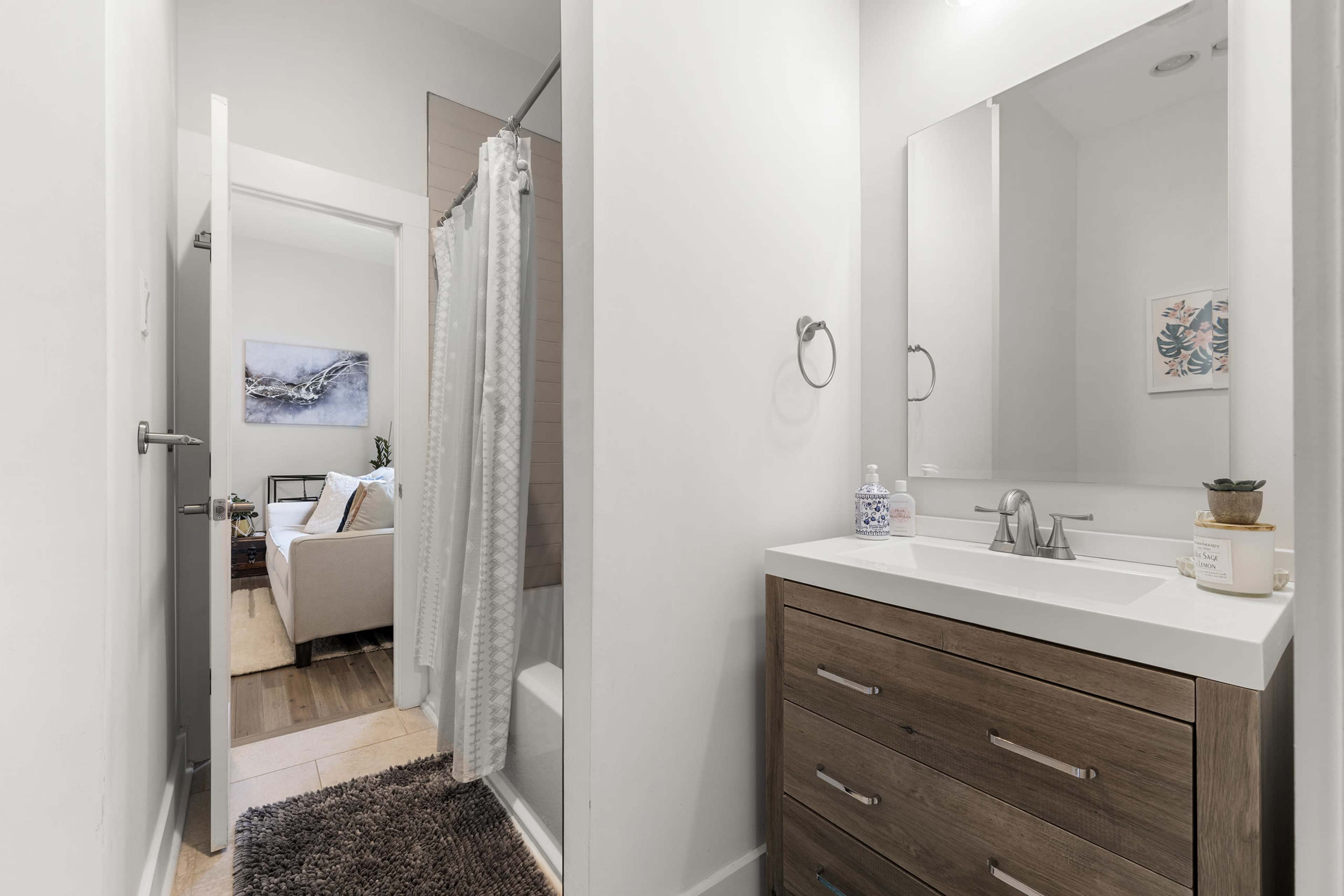 A modern bathroom with a walk-in shower, a vanity with a mirror, and a door leading to a living space in the background.