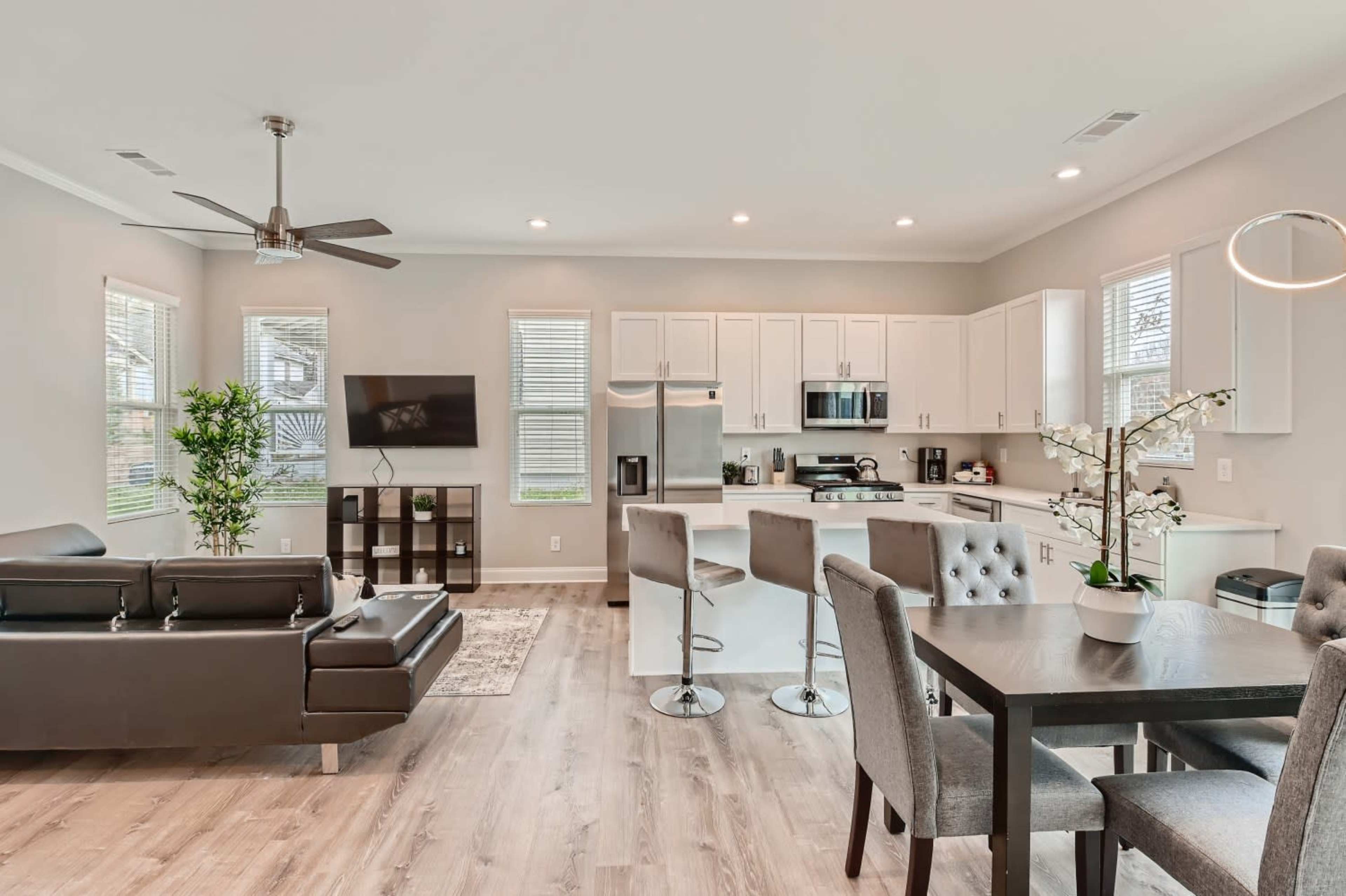 A modern open-concept living space features a kitchen, dining area, and living room with sleek furnishings and large windows.