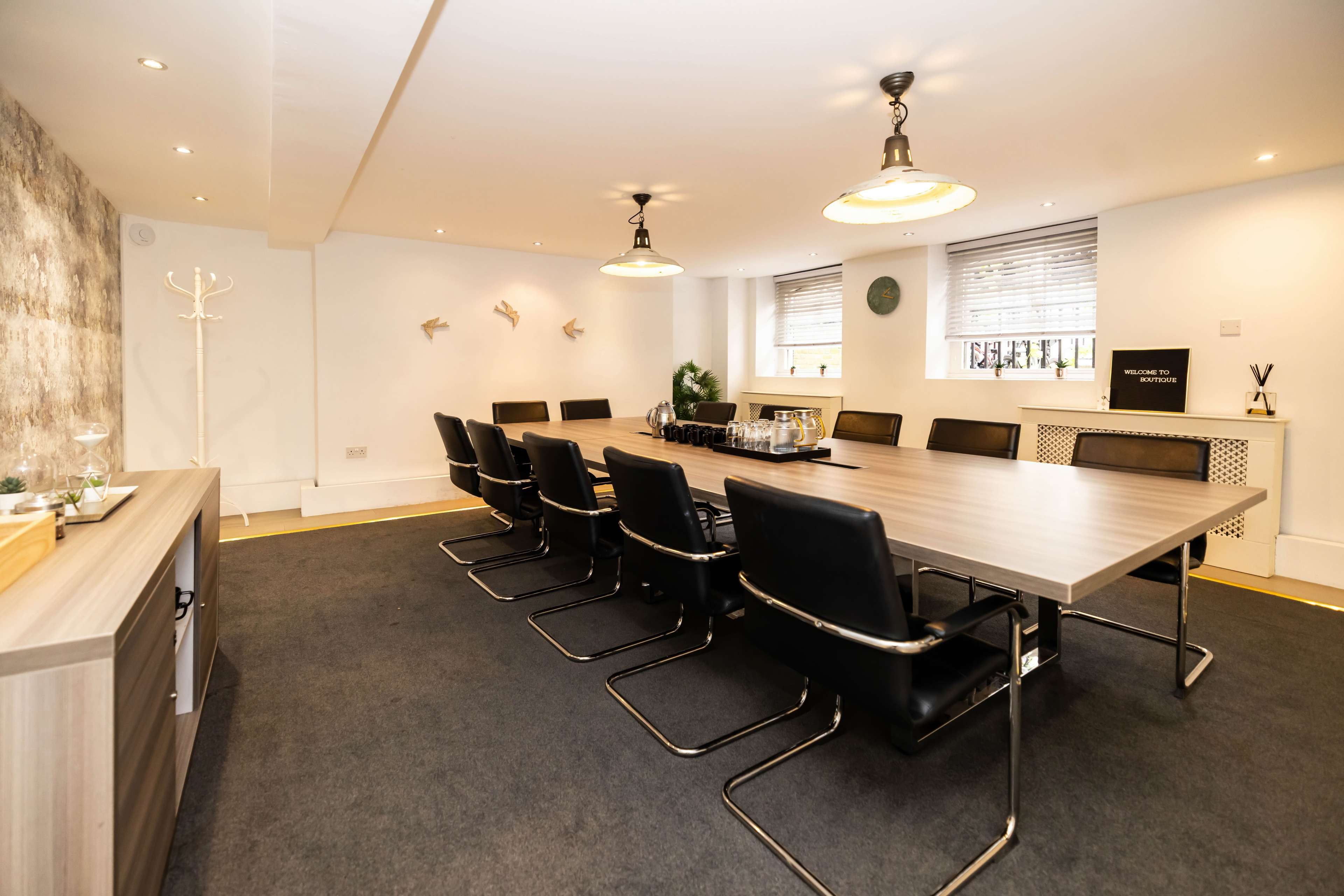 The image shows a spacious conference room with a long wooden table surrounded by black chairs, illuminated by pendant lights.