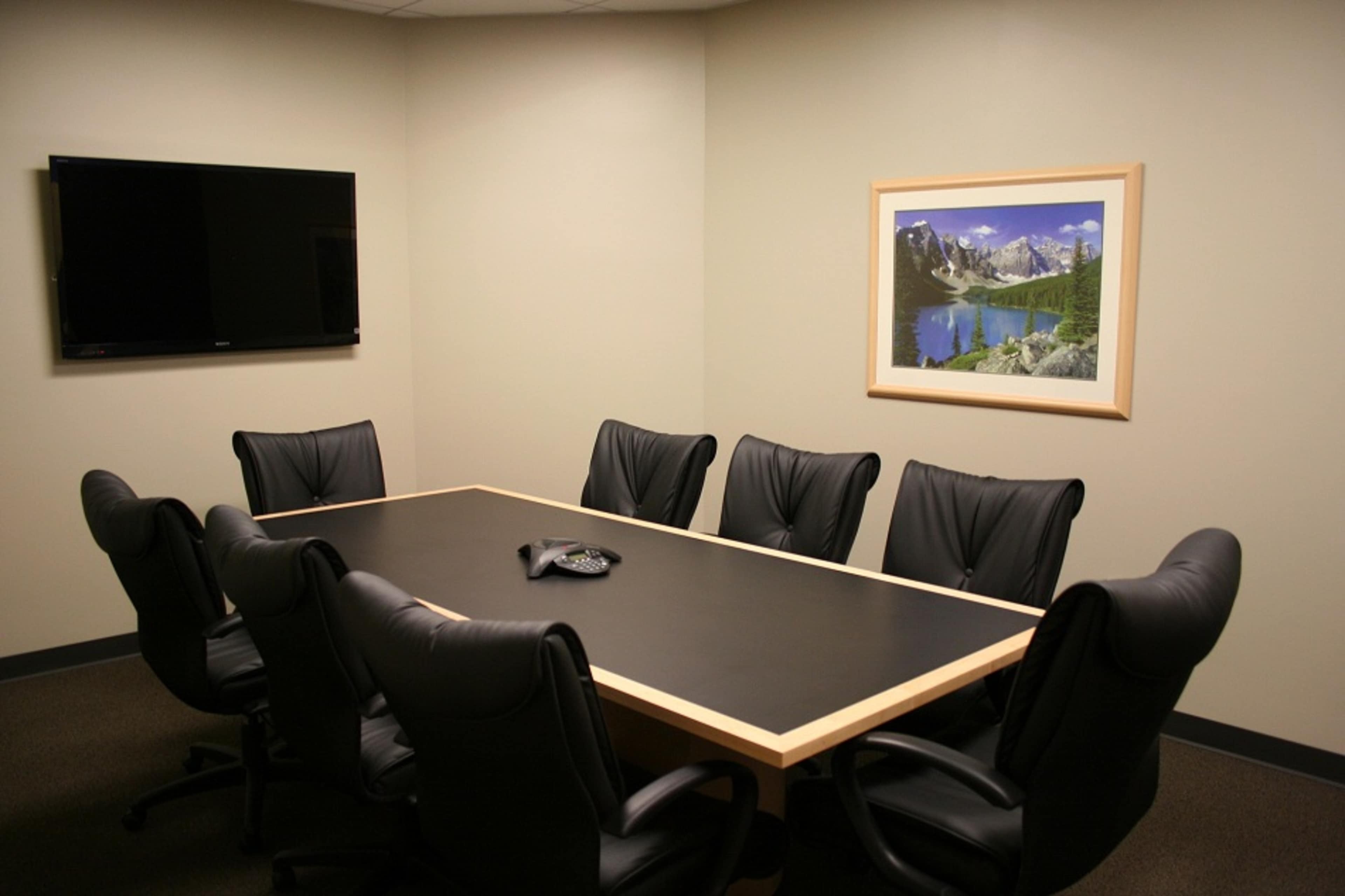 A conference room features a black table surrounded by eight leather chairs, with a television on the wall and a landscape painting framed nearby.