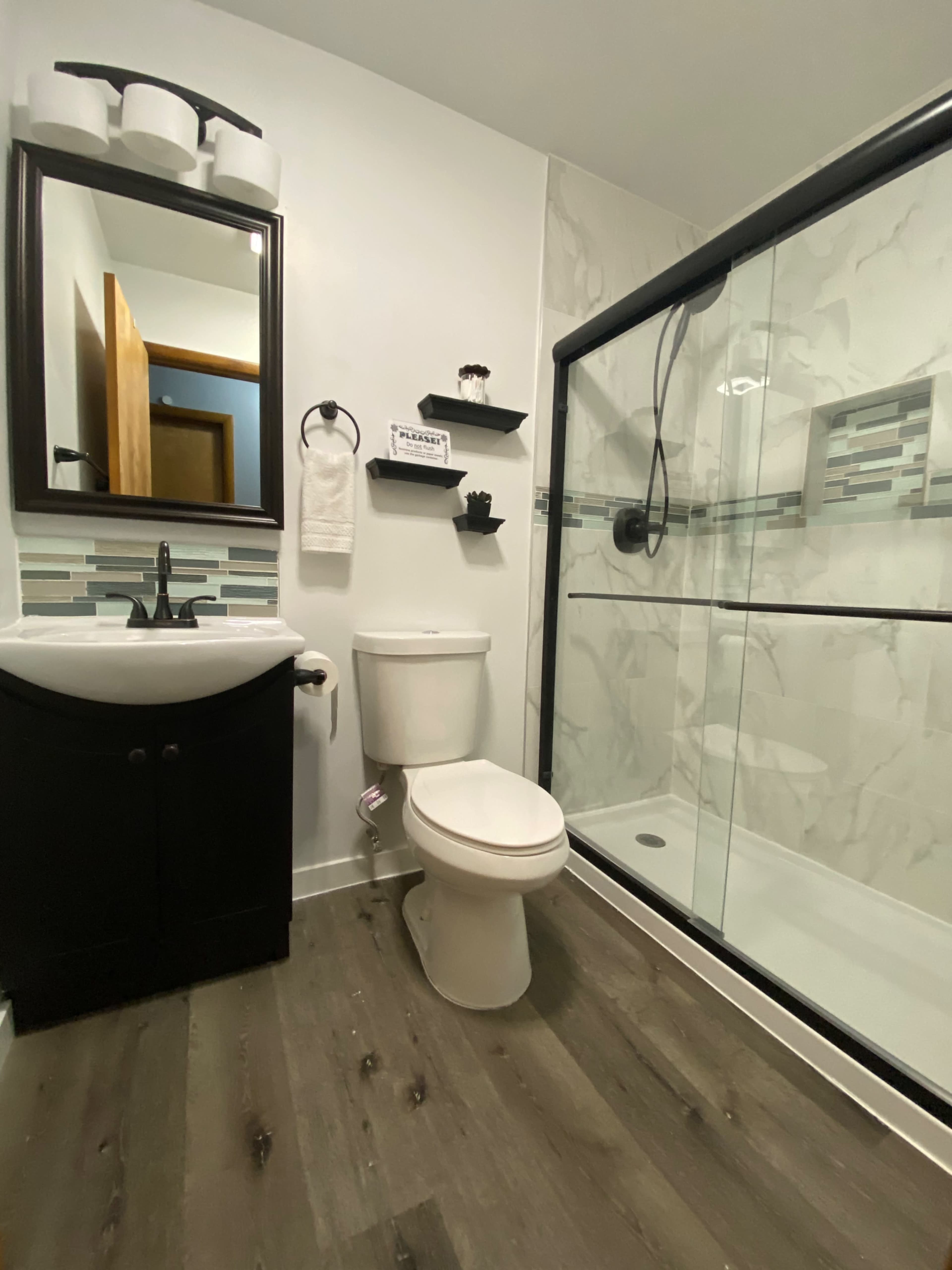 A modern bathroom featuring a shower, toilet, and sink with dark cabinetry and light-colored walls.