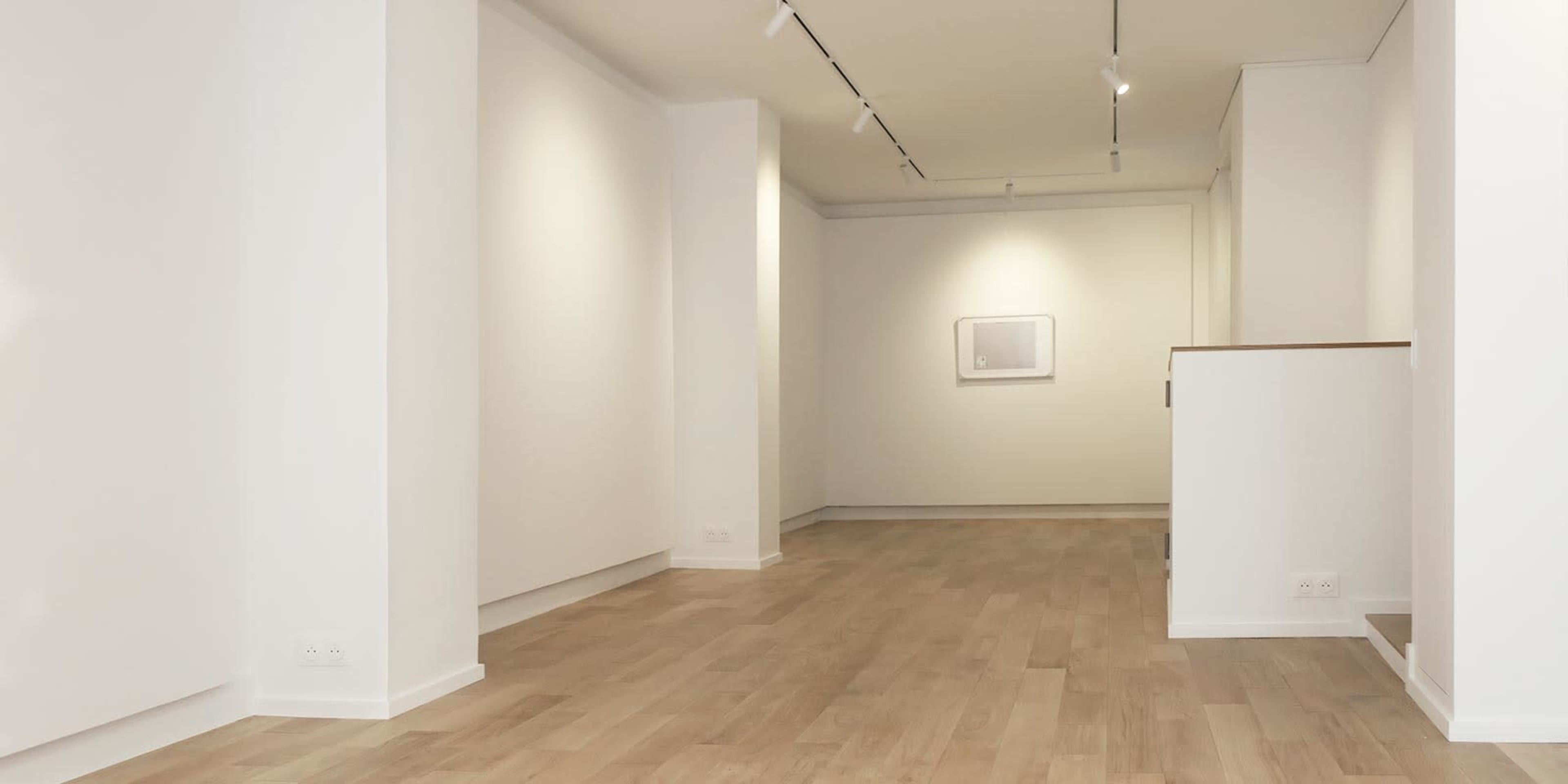 A spacious, empty gallery with light-colored walls and wooden flooring.