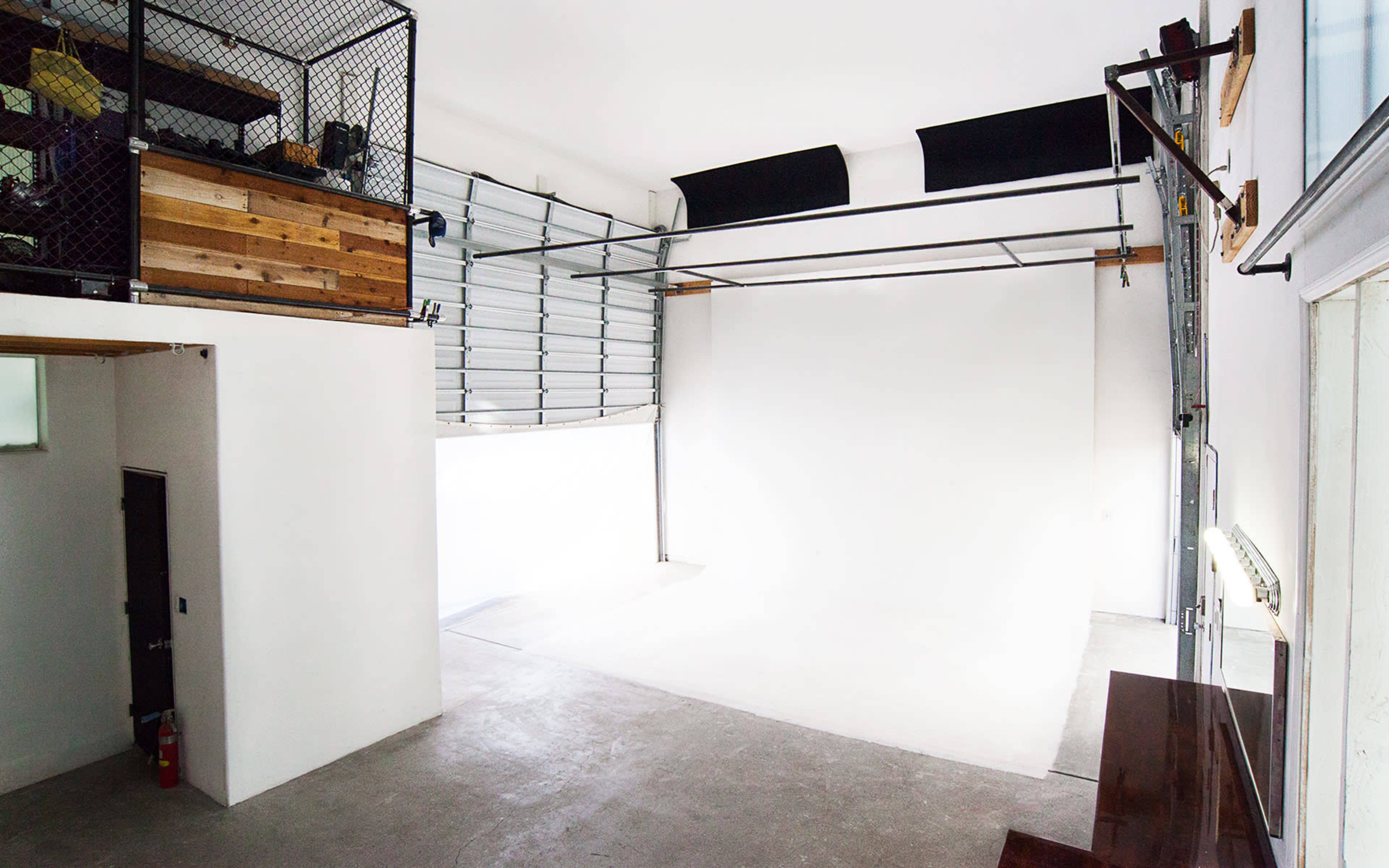 An empty industrial-style room with a high ceiling, a garage door, and a loft area with wooden elements.