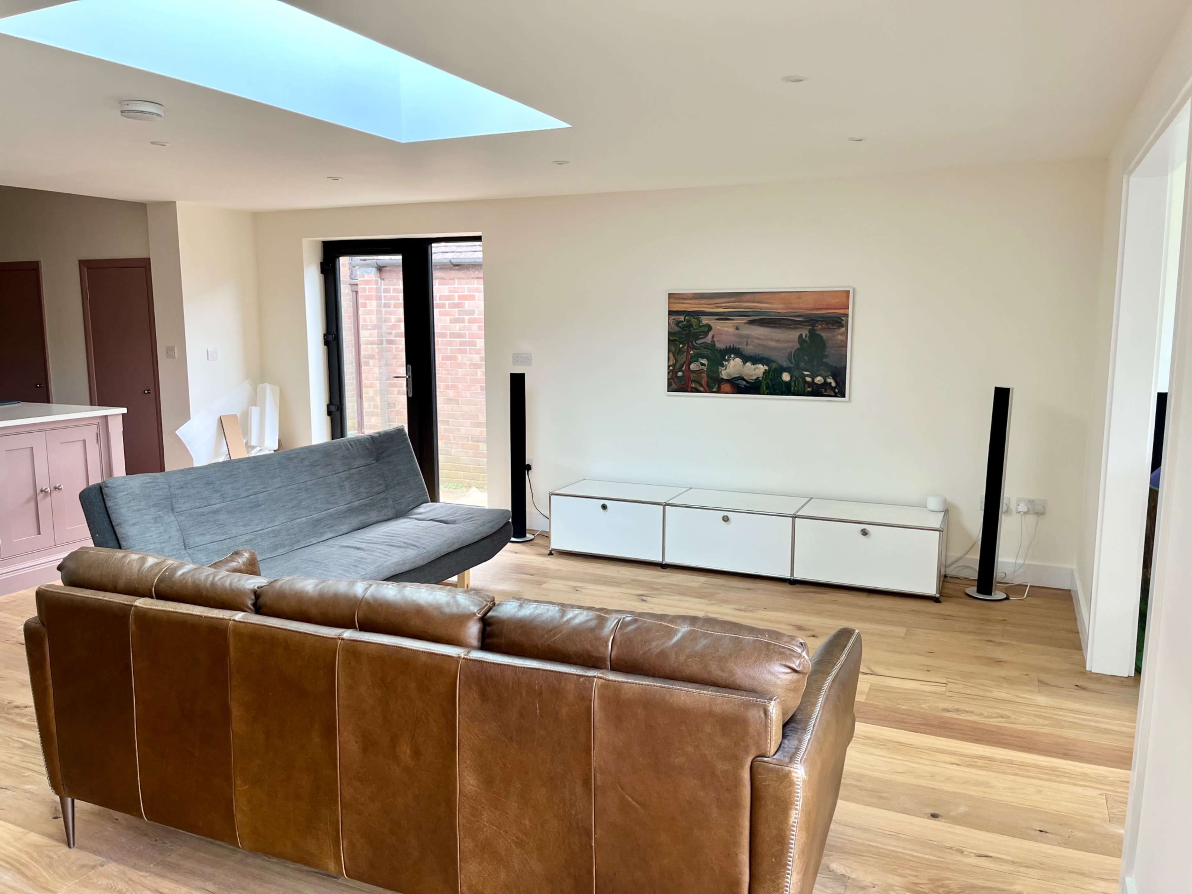 A modern living room features a gray sofa, a brown leather couch, a white entertainment unit, and a painting on the wall.