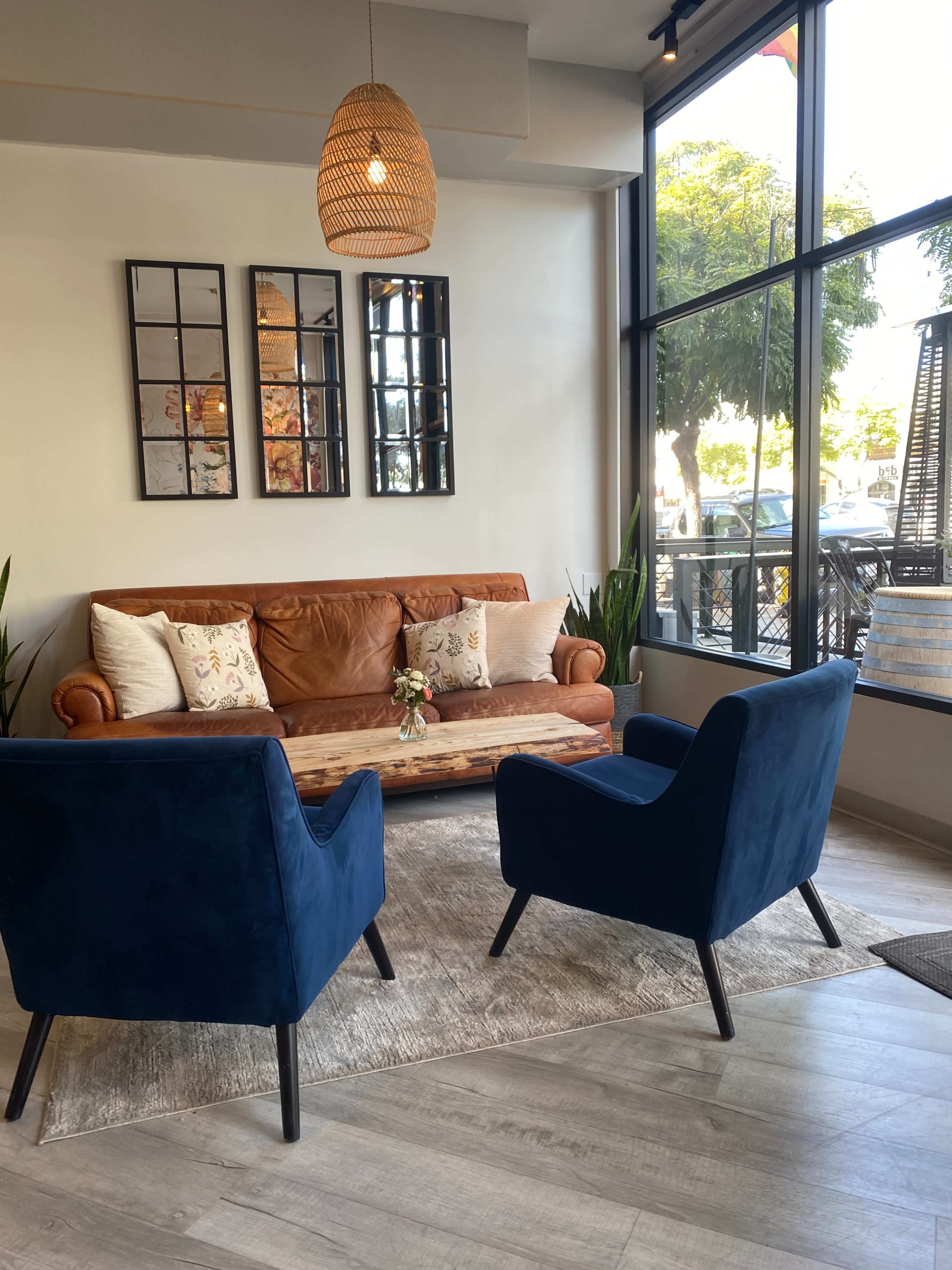 A cozy seating area features a brown leather sofa, two blue chairs, and a wooden coffee table under a hanging light fixture.