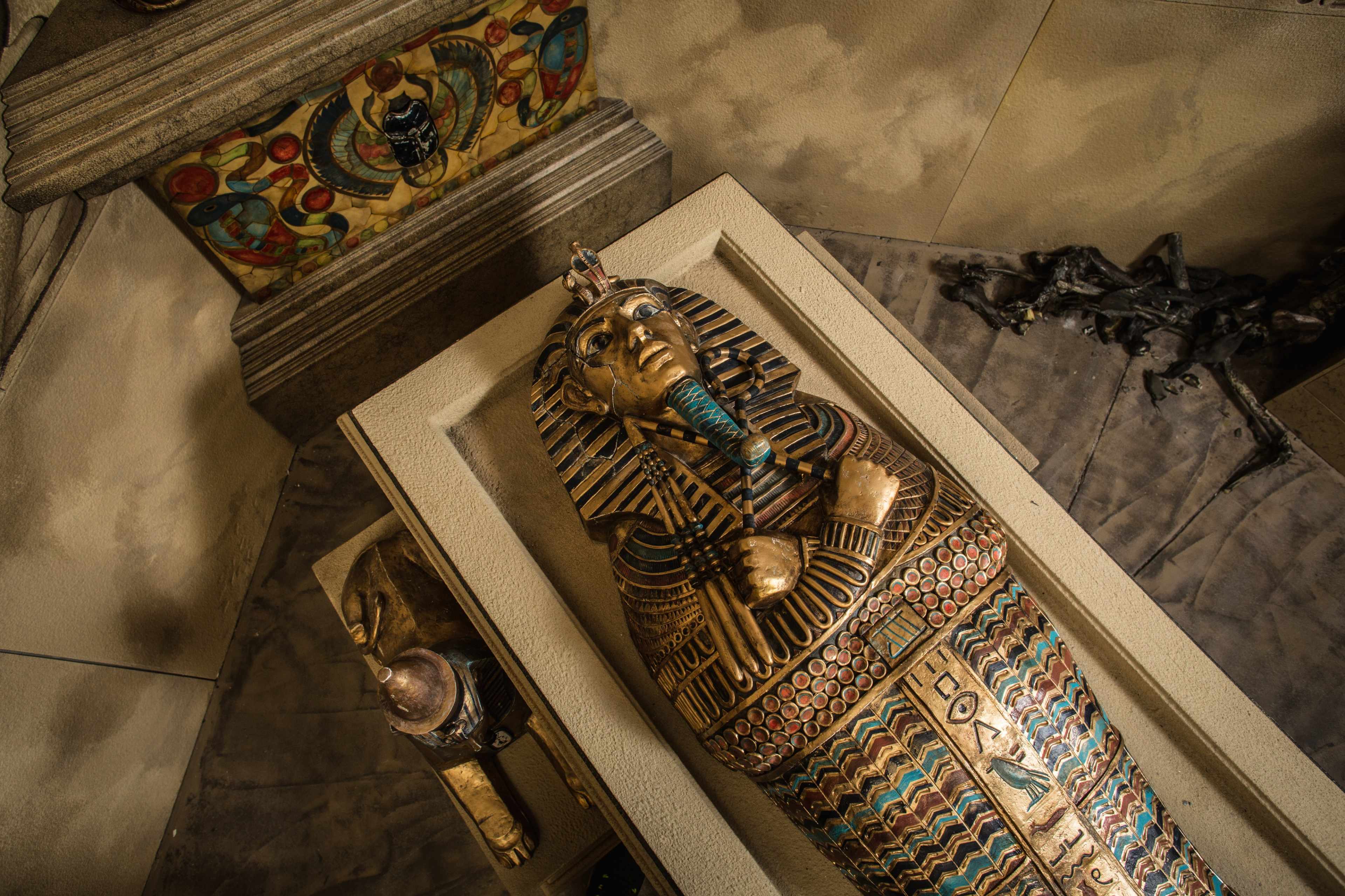 A detailed view of a decorated ancient Egyptian sarcophagus placed within a tomb setting.