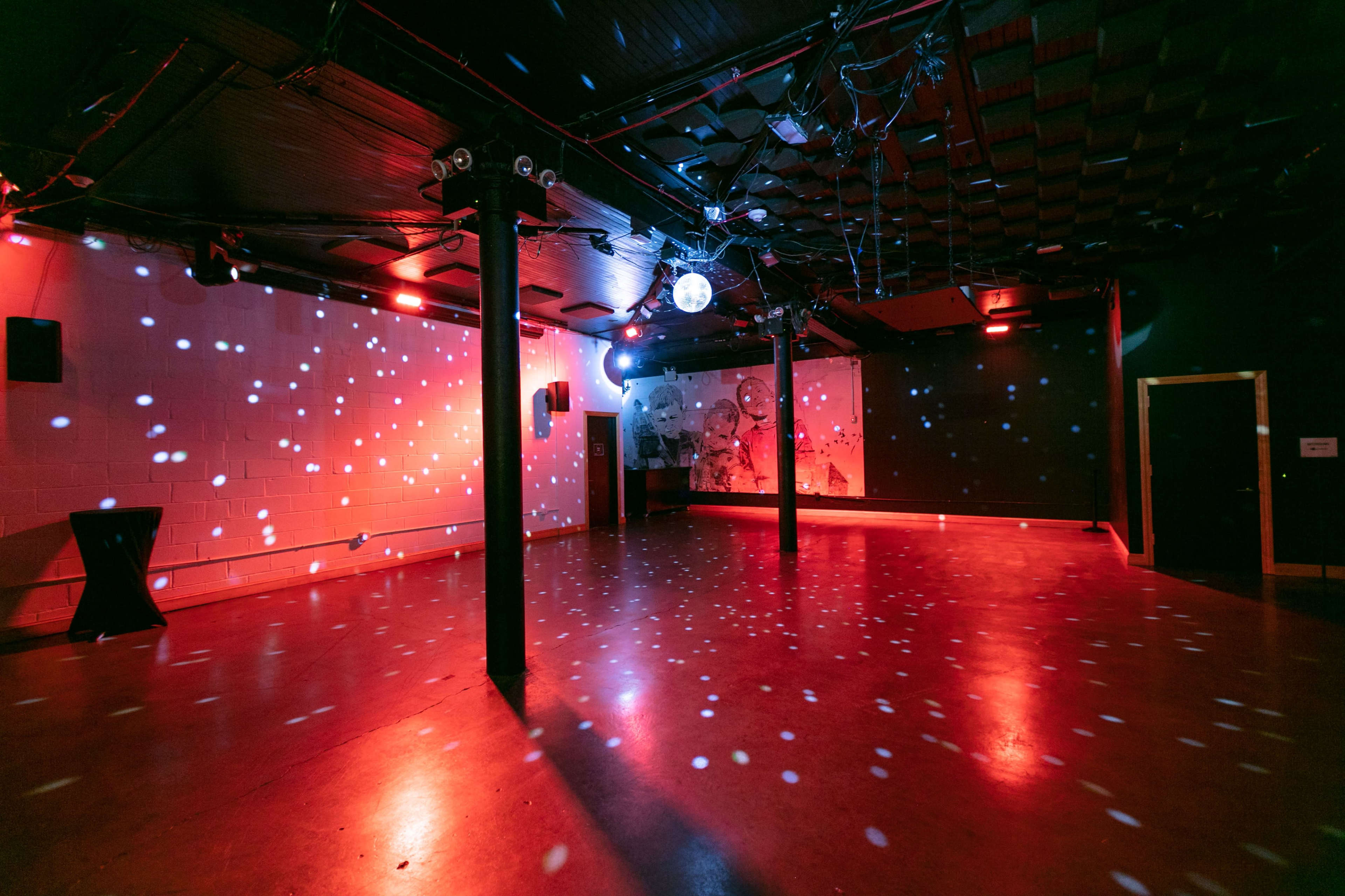 A dimly lit event space features colored lights and a disco ball reflecting patterns on the floor and walls.