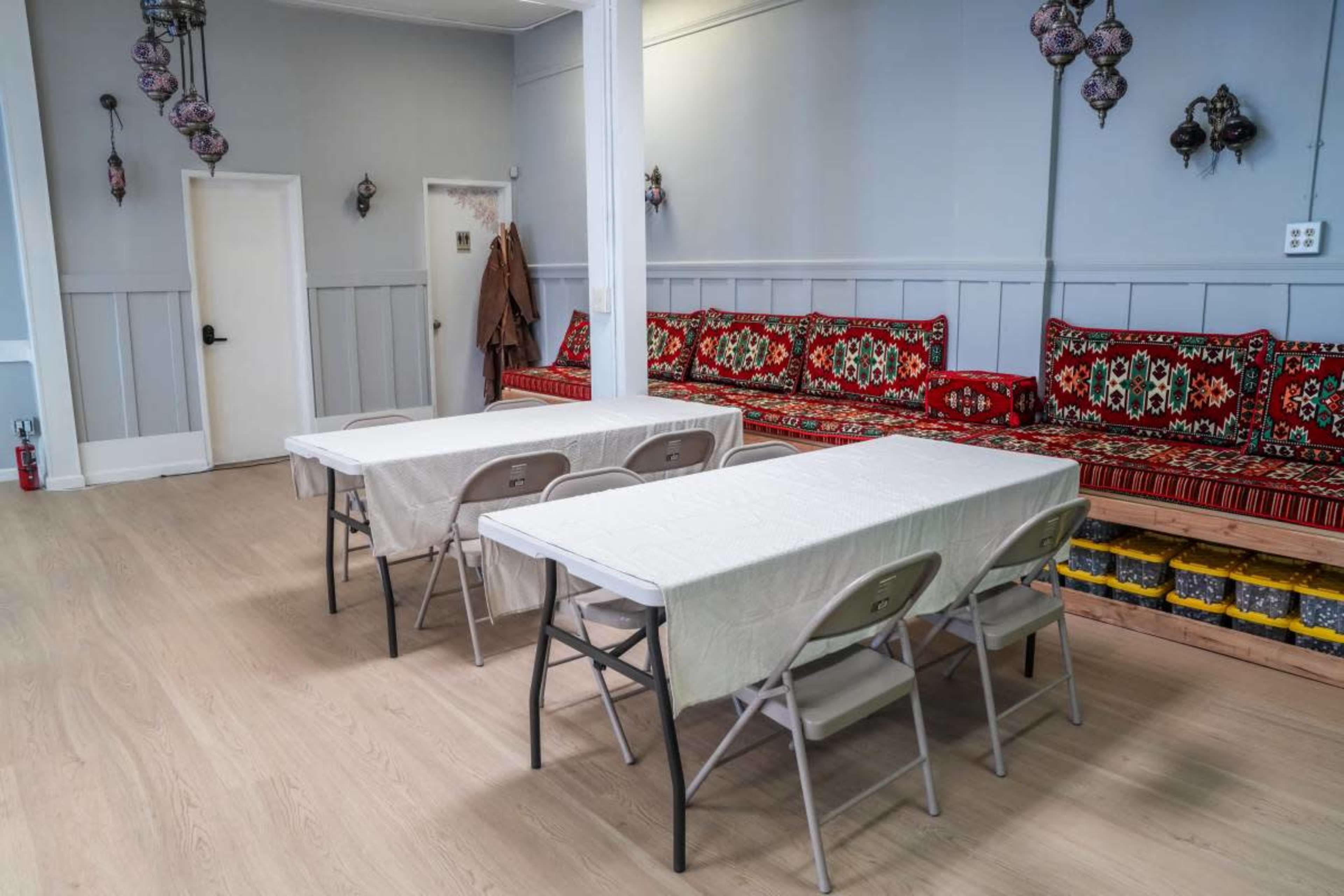 The image shows a room with two folding tables set for seating, surrounded by a couch with patterned upholstery and decorative lanterns hanging from the ceiling.