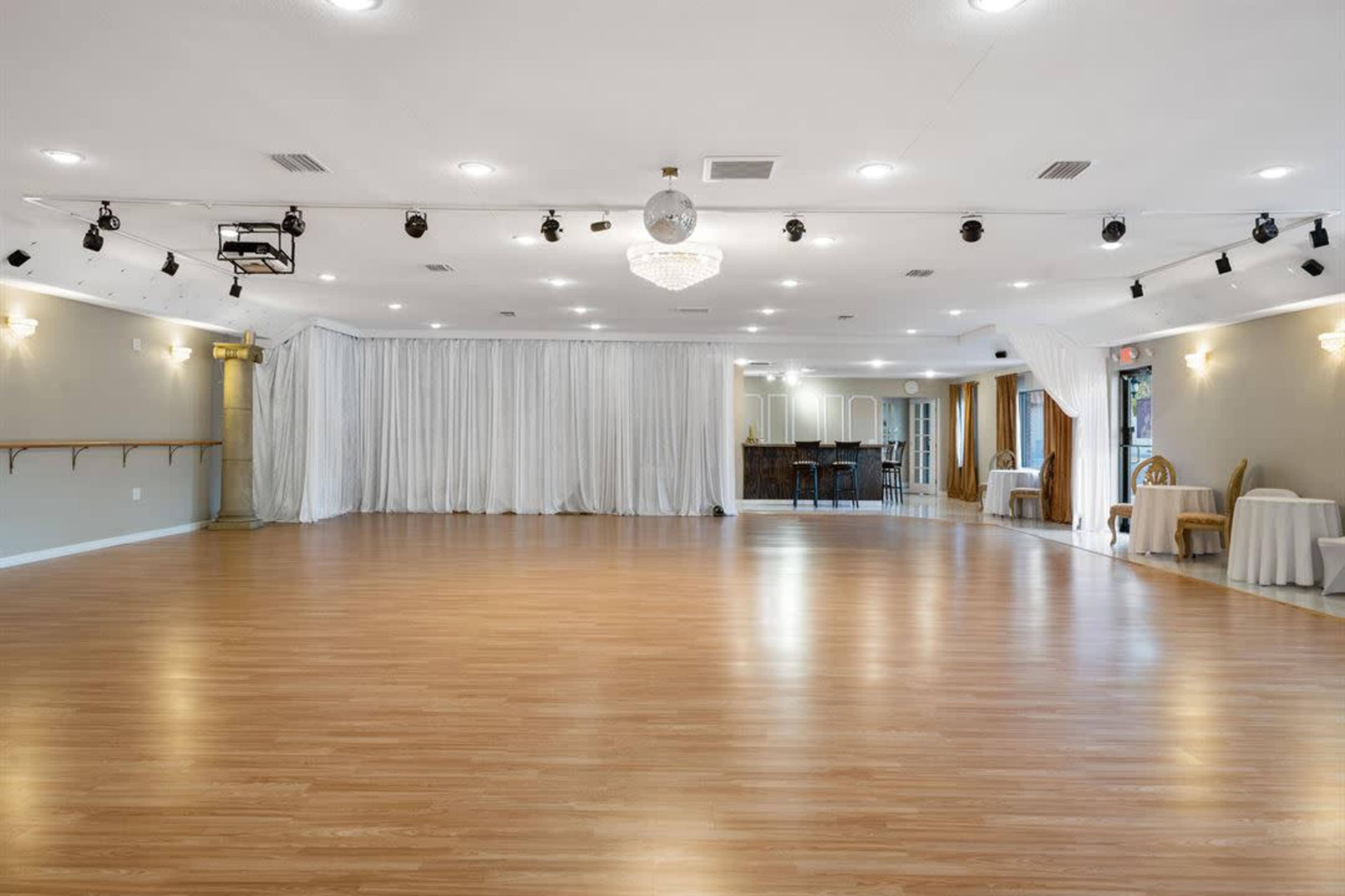 The image shows a spacious empty dance studio with wooden flooring,several light fixtures, and curtains in the background.