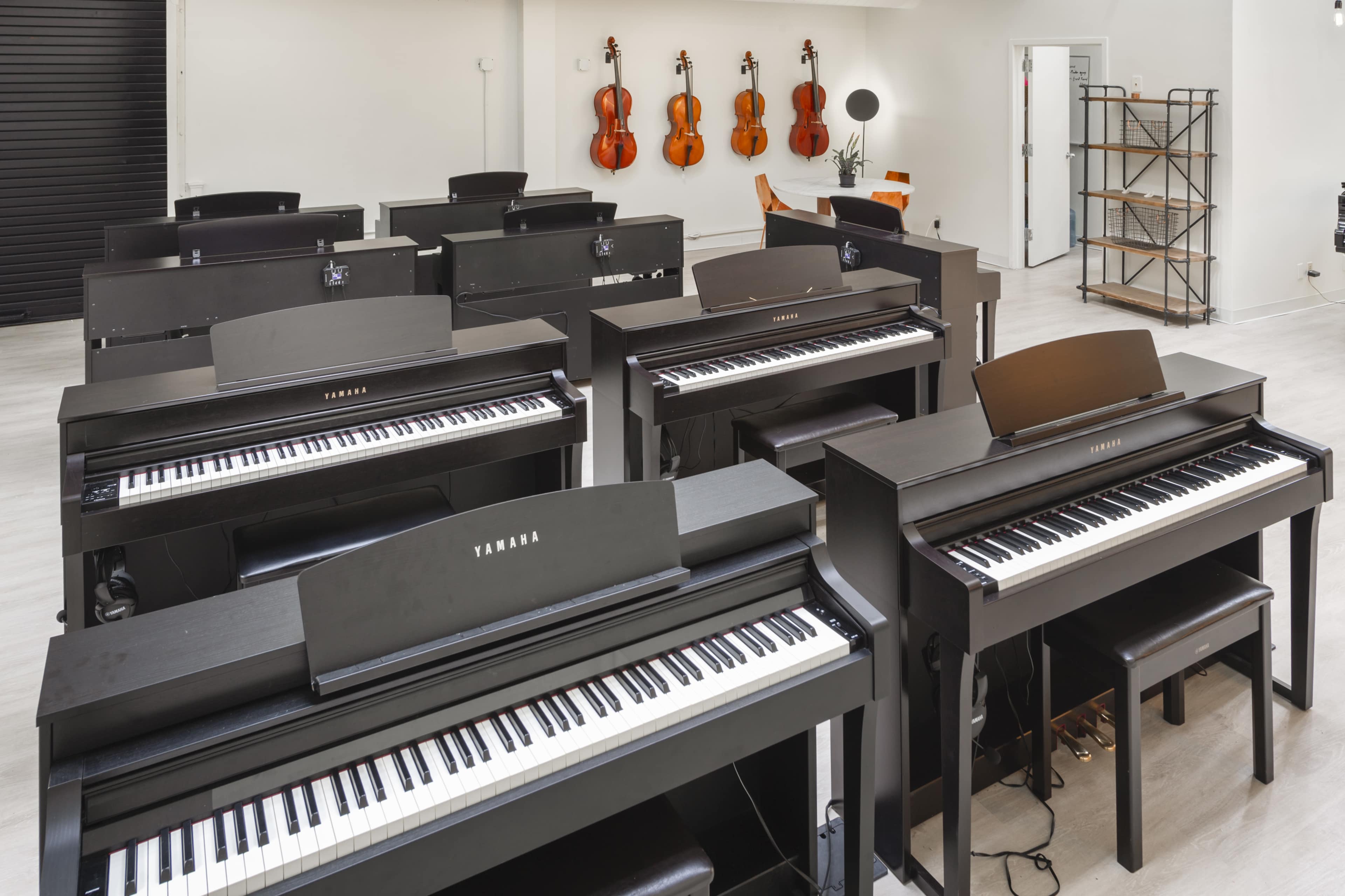 A music store interior featuring multiple black digital pianos arranged in rows, with violins hanging on the wall in the background.