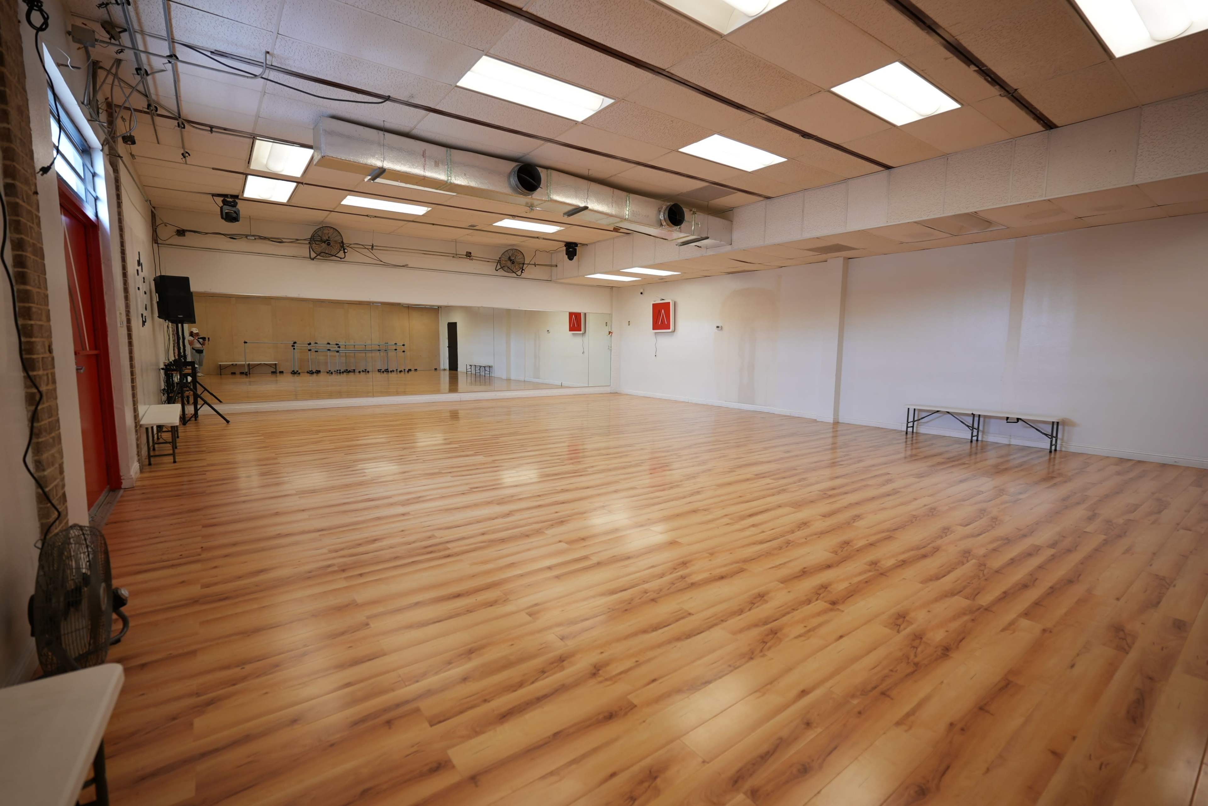 The image shows a spacious dance studio featuring wooden floors, mirrors along one wall, and a small table set up in the corner.