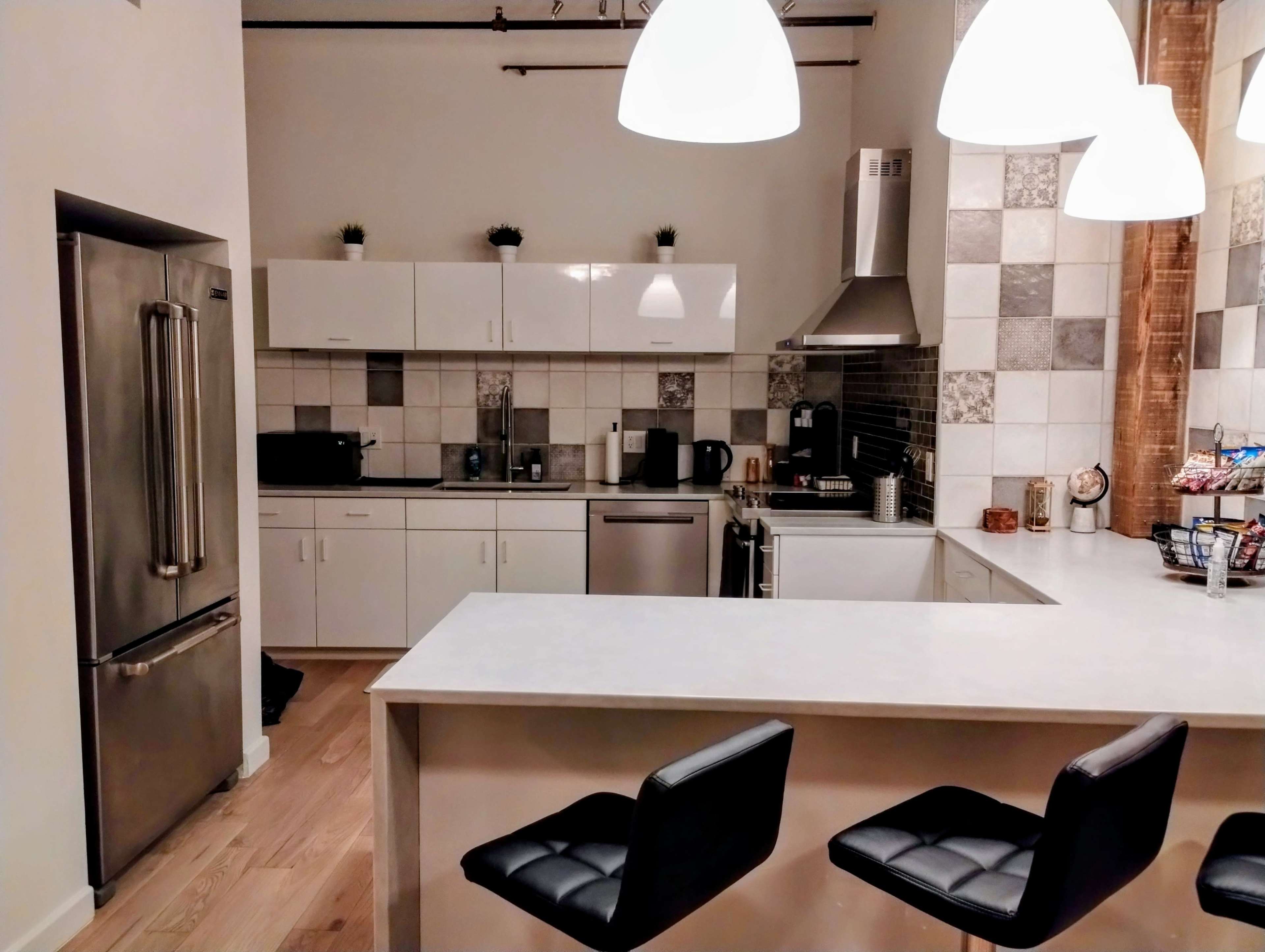 A modern kitchen with white cabinets, a silver refrigerator, and a bar area with black stools.