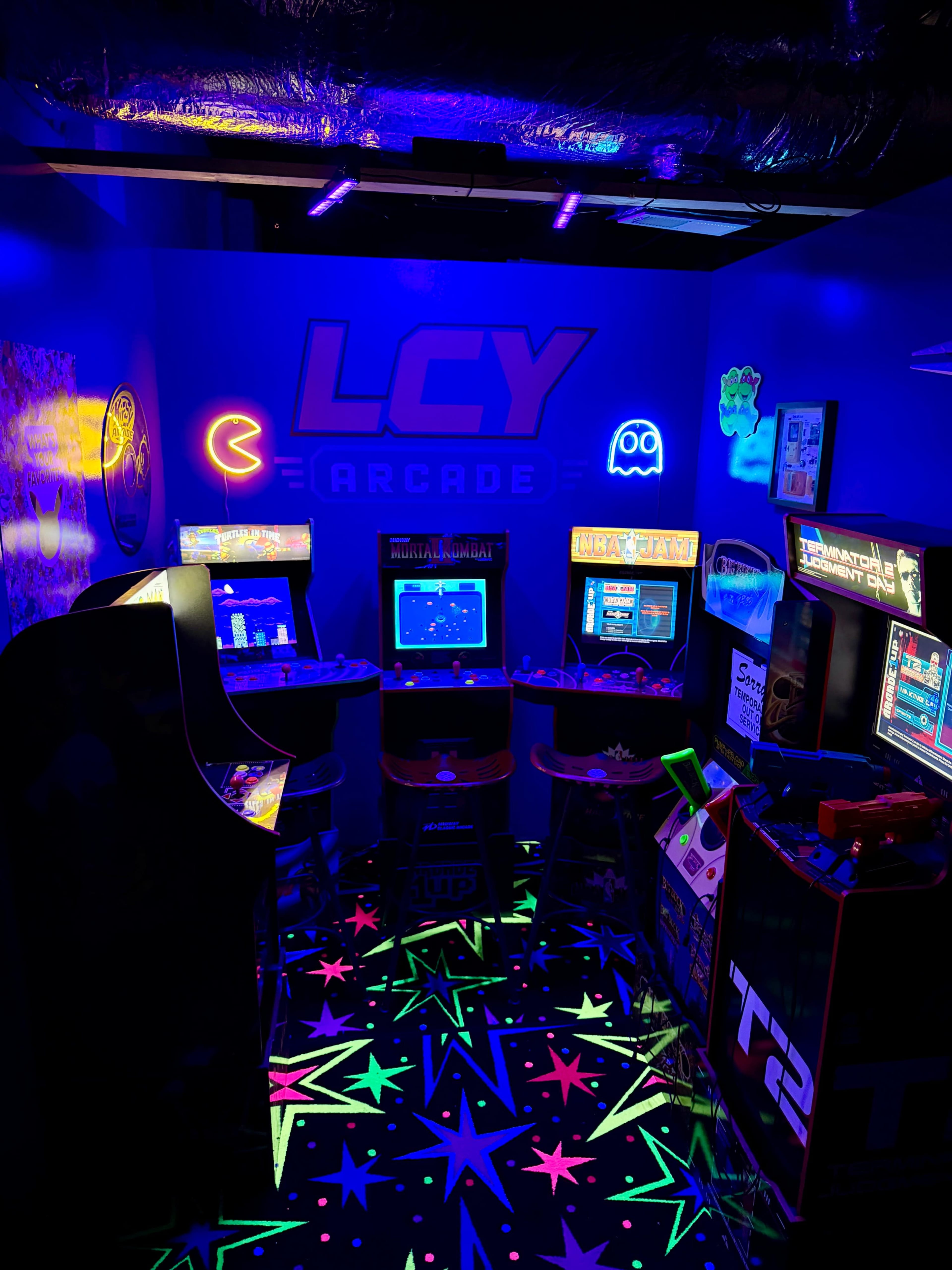 The image shows a brightly lit arcade room filled with vintage arcade machines and colorful star-patterned flooring under blacklight.