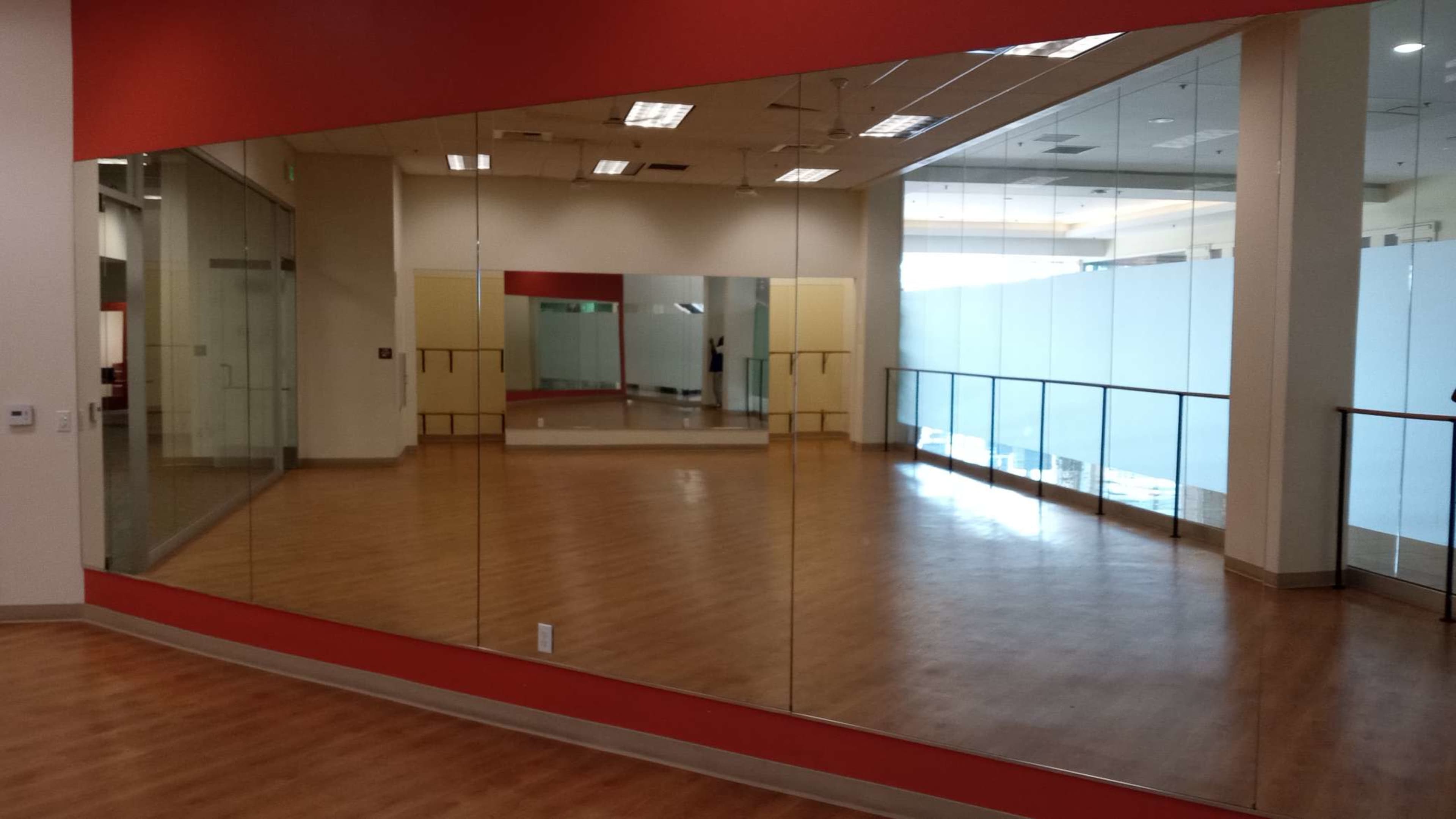 A spacious room with mirrored walls and wooden flooring, featuring large windows that provide natural light.