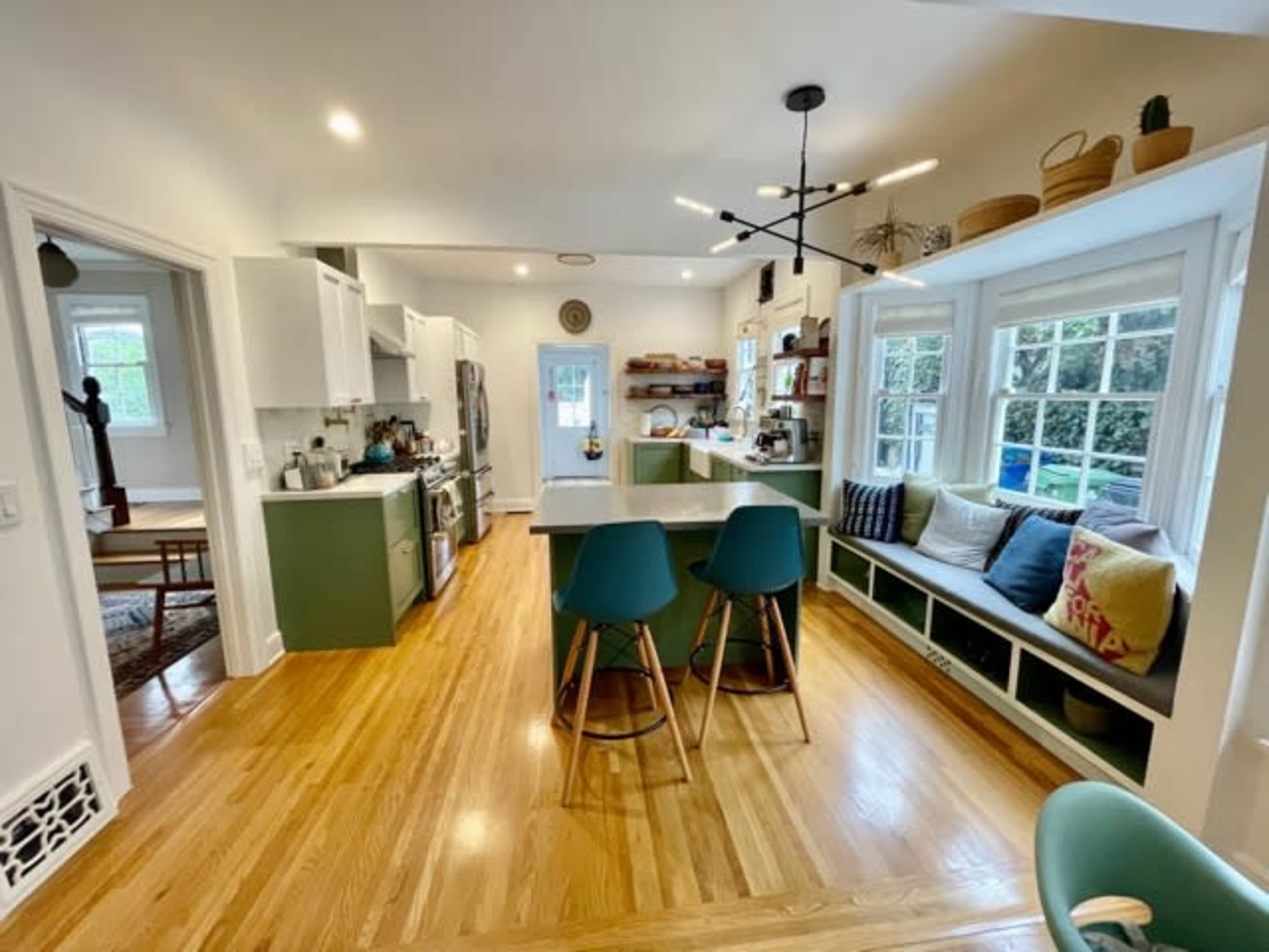 A modern kitchen with green cabinetry, a large island with bar seating, and a cozy window nook filled with cushions.