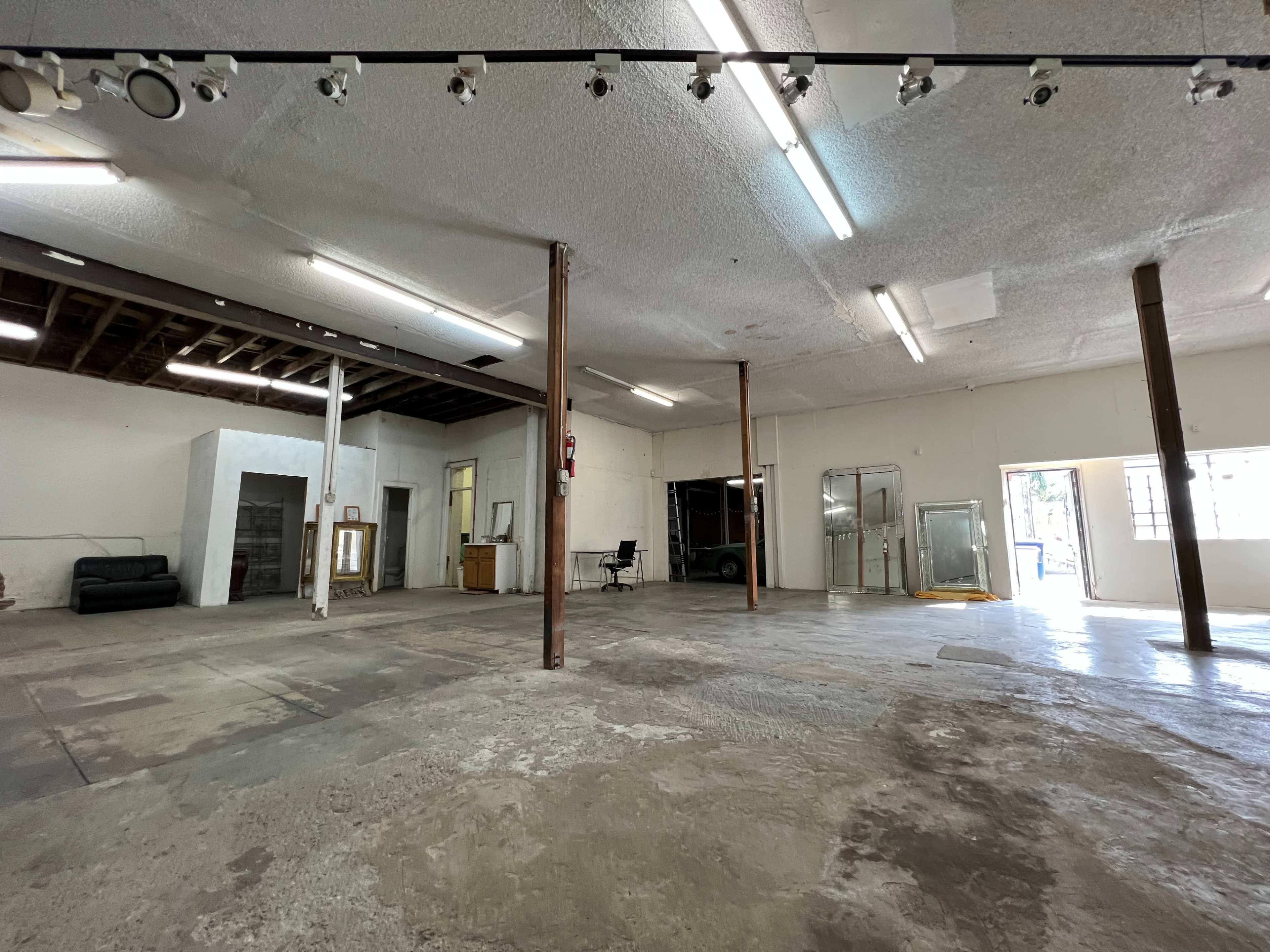 An empty warehouse space with concrete flooring, exposed wooden beams, and large windows.