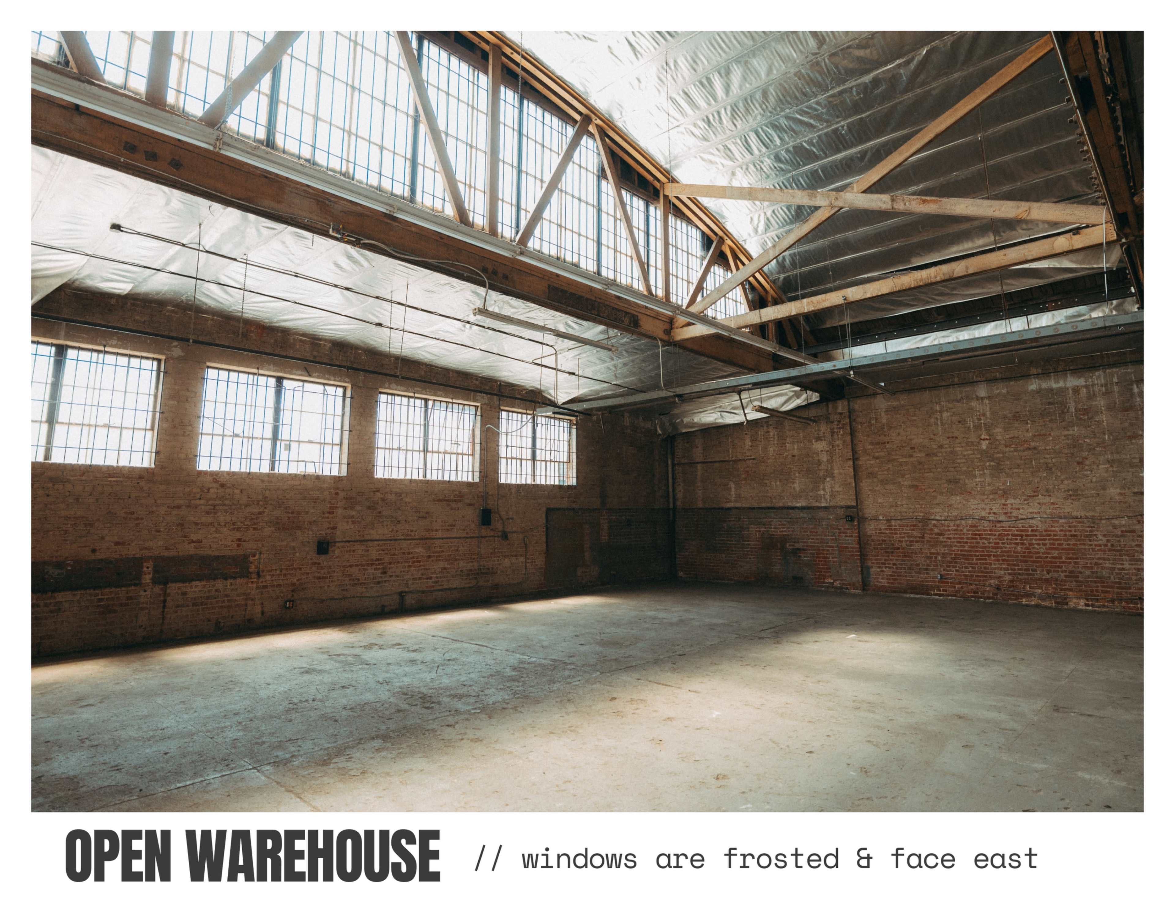 An open warehouse features frosted windows that face east, with exposed brick walls and a clear floor space.