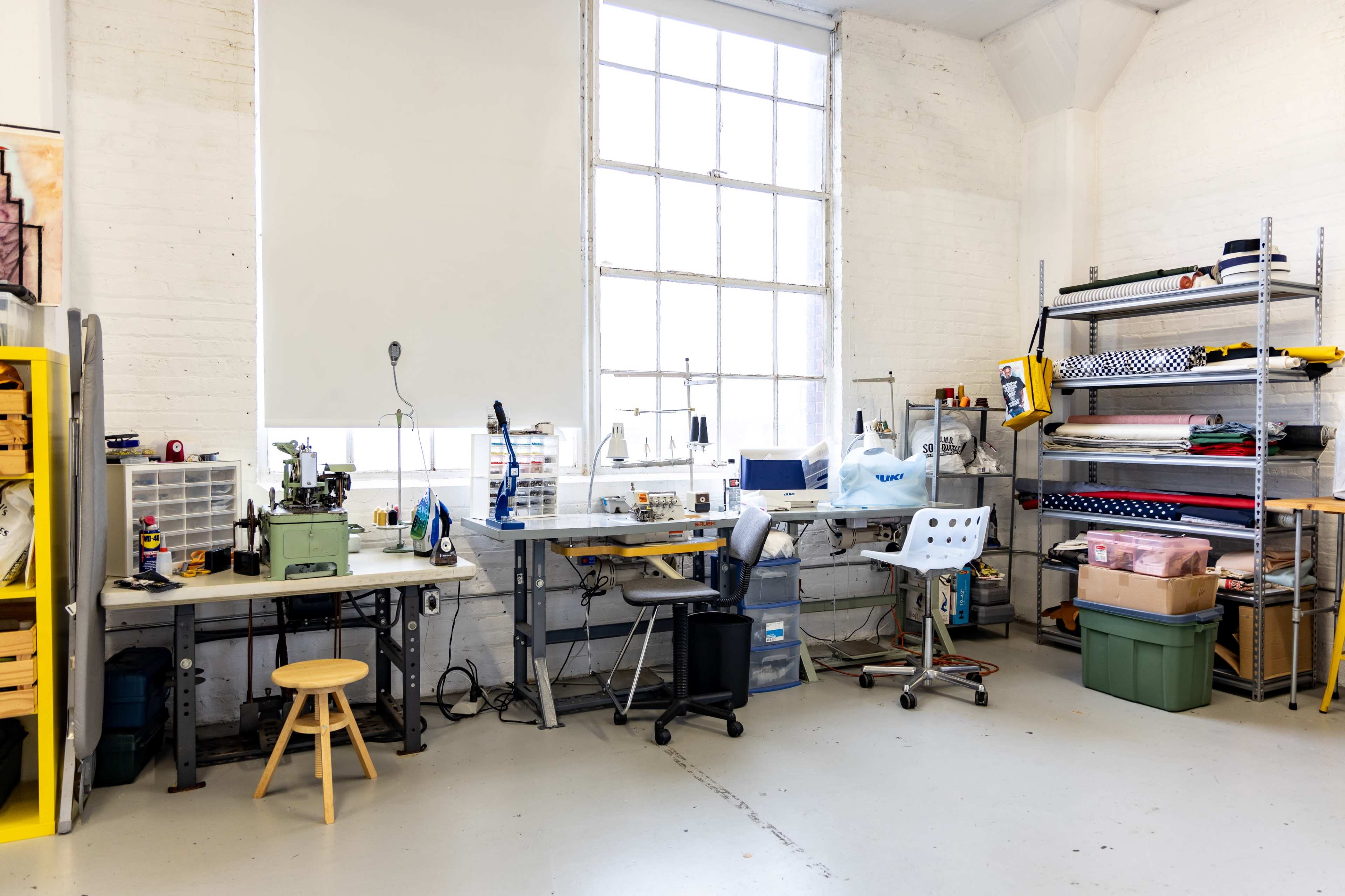 A bright workshop with several workstations, shelving units, and a large window allowing natural light to enter.