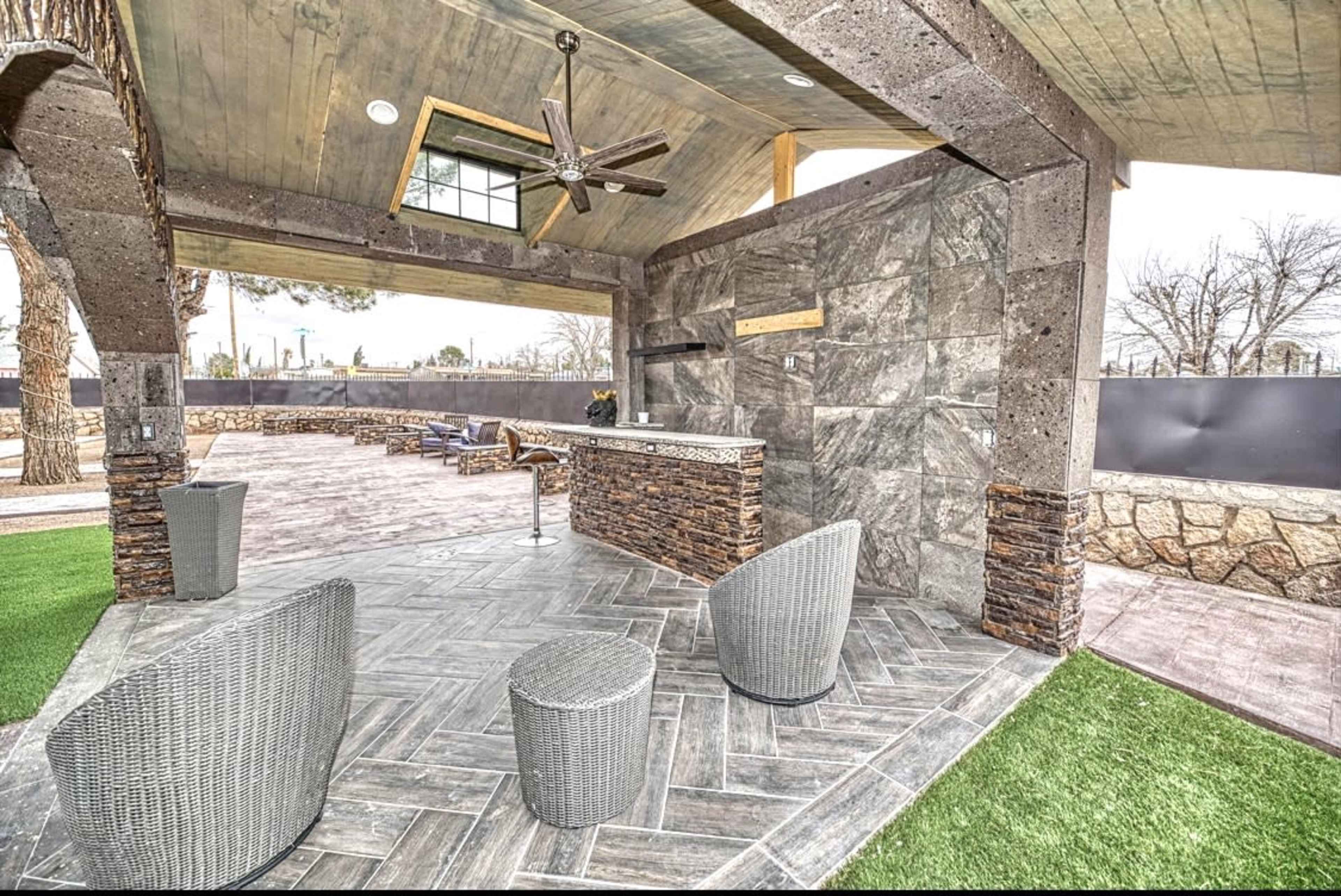 An outdoor patio area featuring a stone bar with seating, surrounded by landscaped grass and a covered roof.